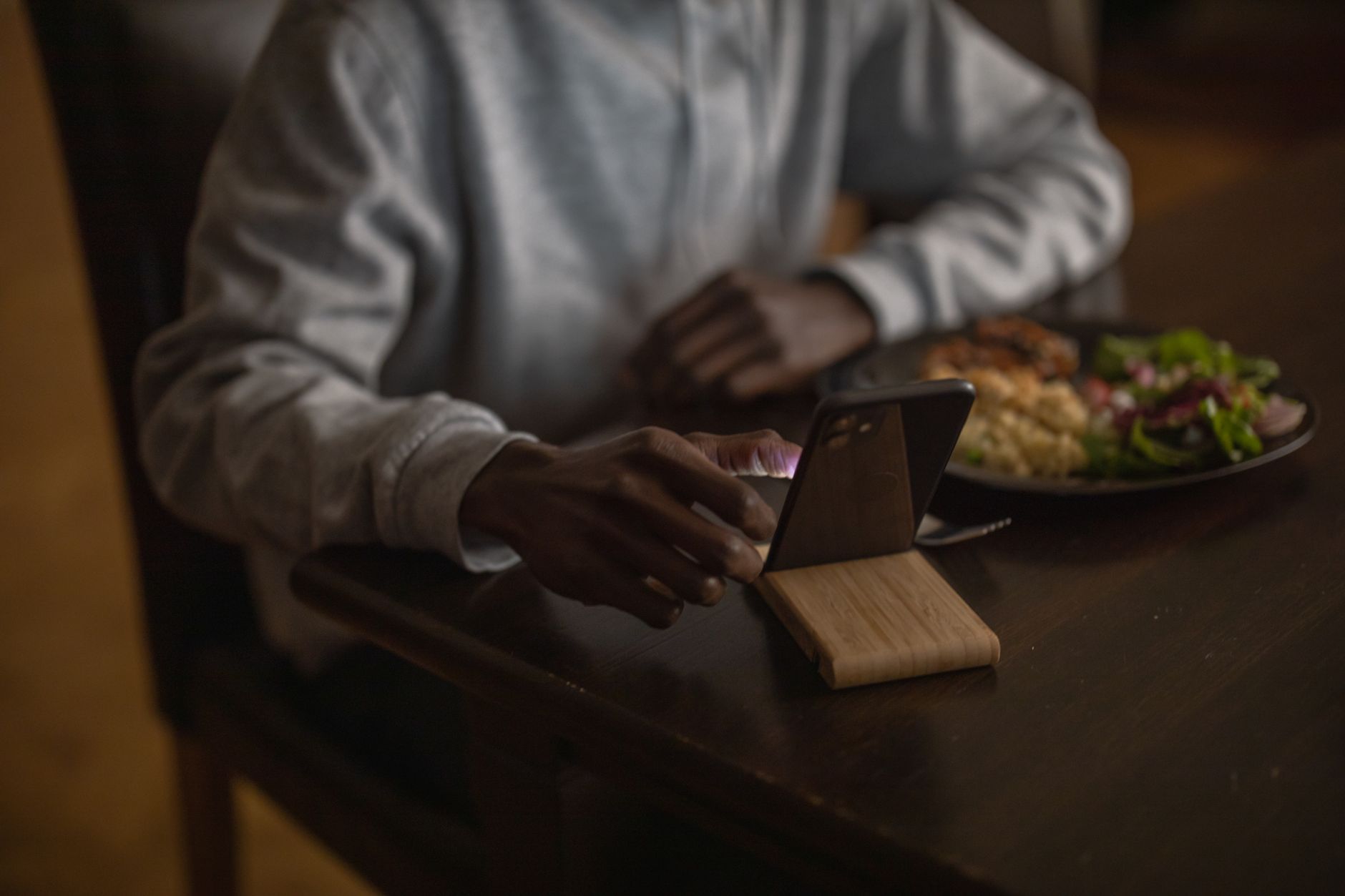 Pessoa segurando um celular ao lado de um carregador sobre uma mesa