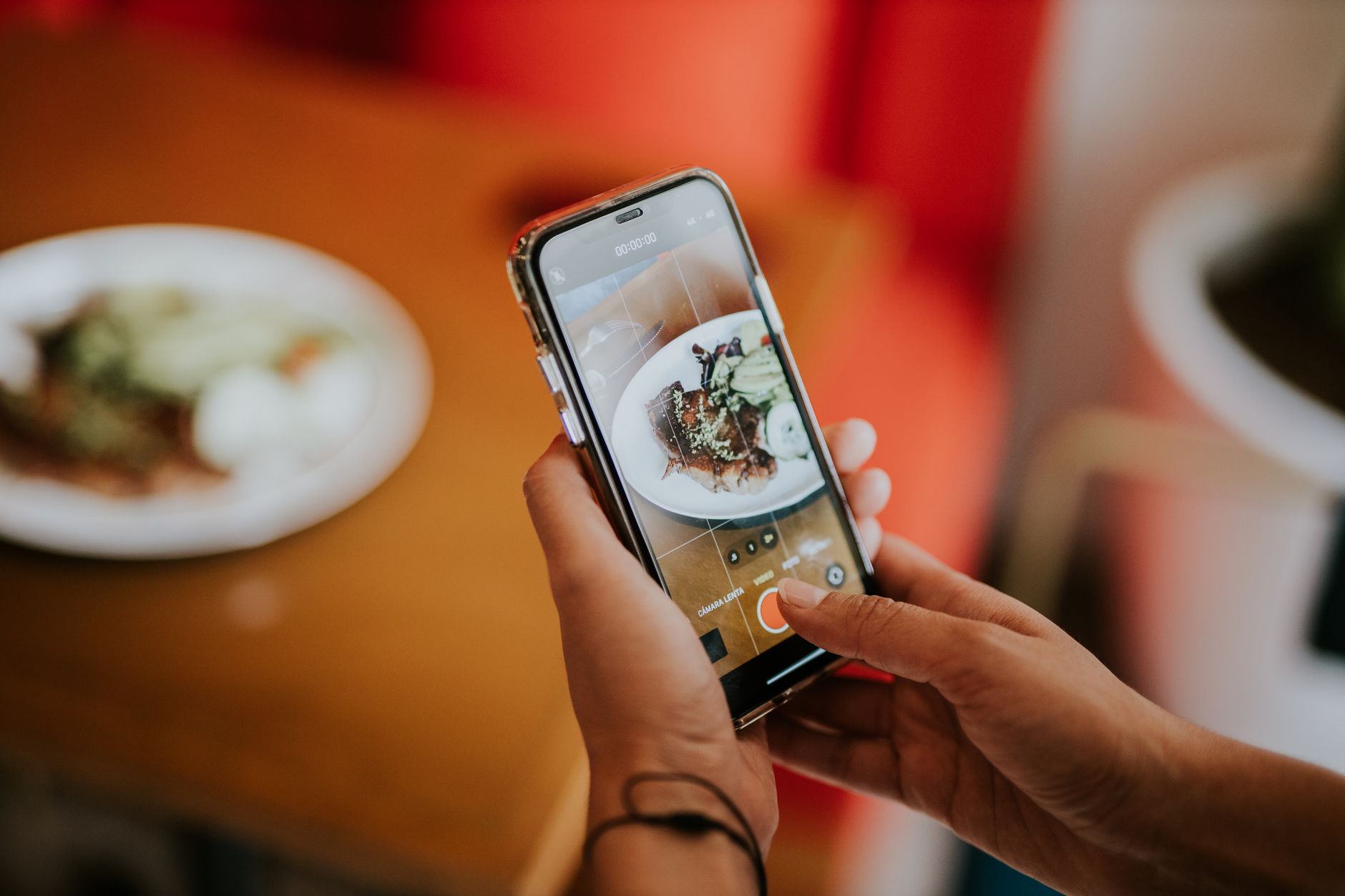 iPhone 16: análise completa para quem vem de um antigo Close-up of a person using a smartphone to photograph food in a cozy indoor setting.