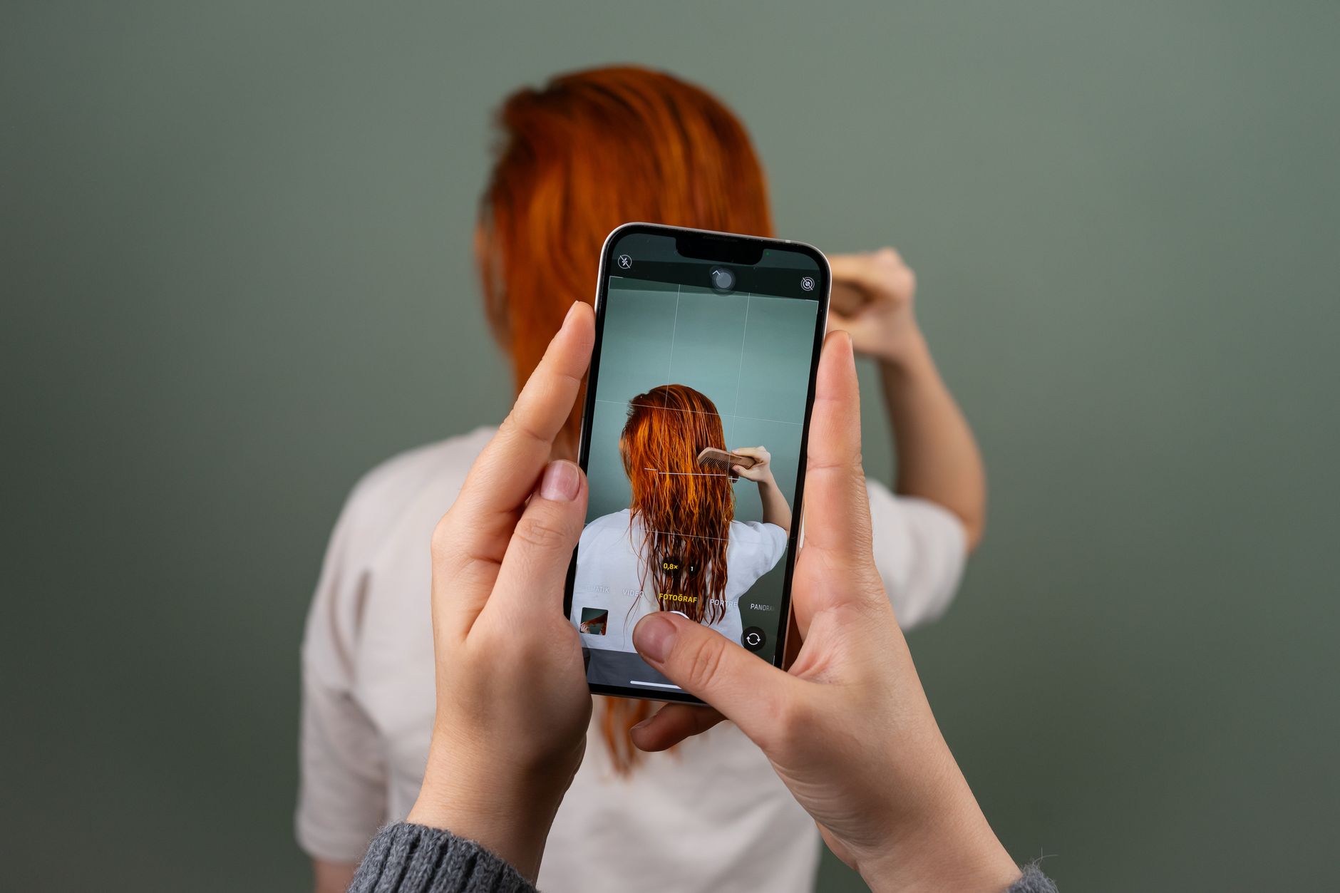 iPhone 16e: análise dos cortes no uso diário Photographing a person with red hair using a smartphone indoors.