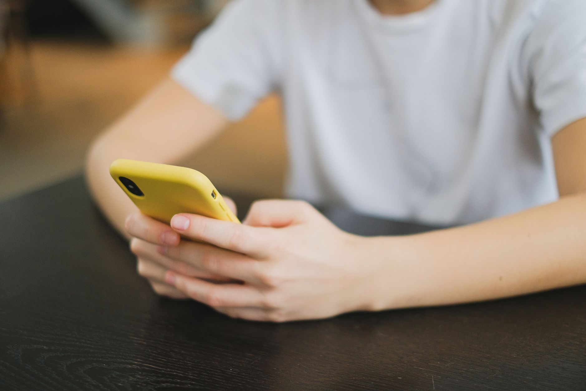 Pessoa segurando um celular diante de uma mesa com ficha técnica e acessórios.