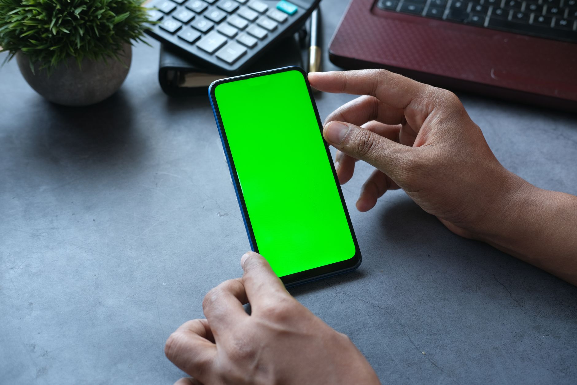 Pessoa segurando um smartphone moderno em uma mesa de trabalho.