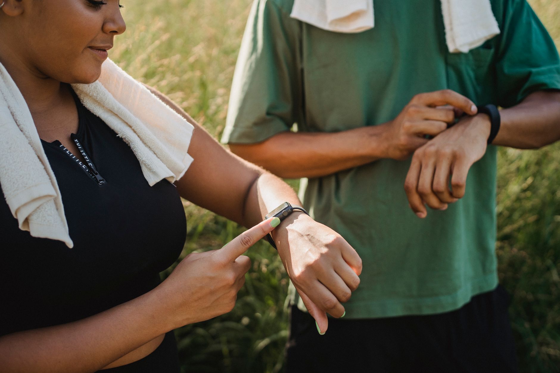 Como escolher entre Galaxy Watch e Apple Watch Two people checking their fitness watches while taking a break from a workout outside.