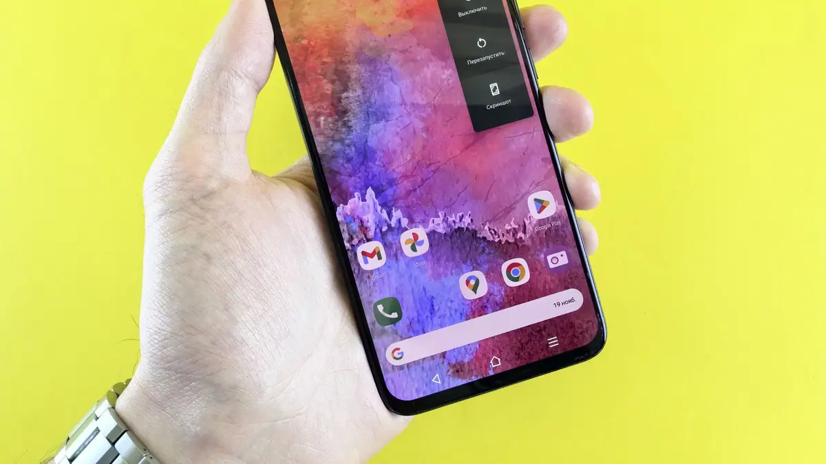 Mão segurando um smartphone com papel de parede colorido sobre fundo amarelo