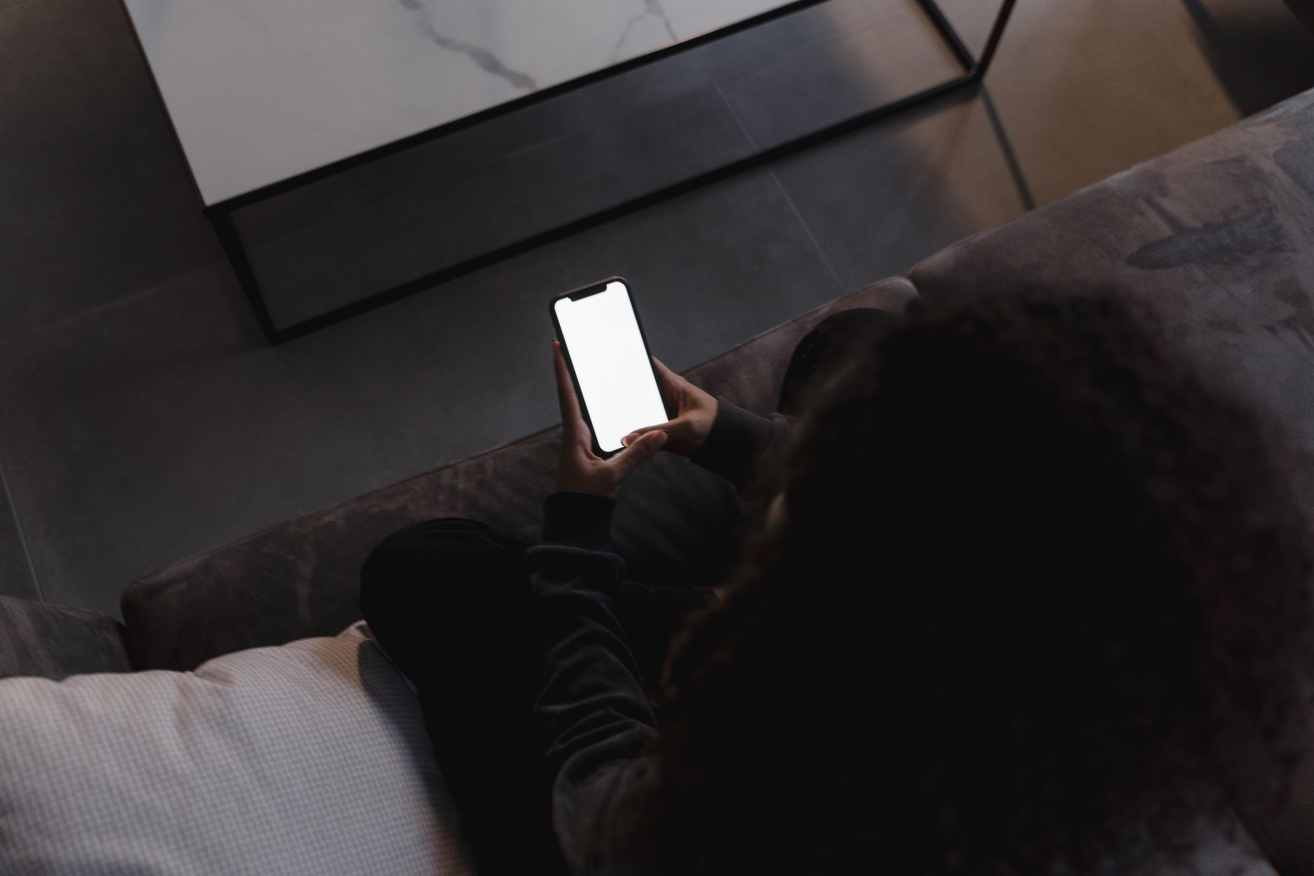 Pessoa segurando um celular com tela OLED acesa em uma sala bem iluminada.