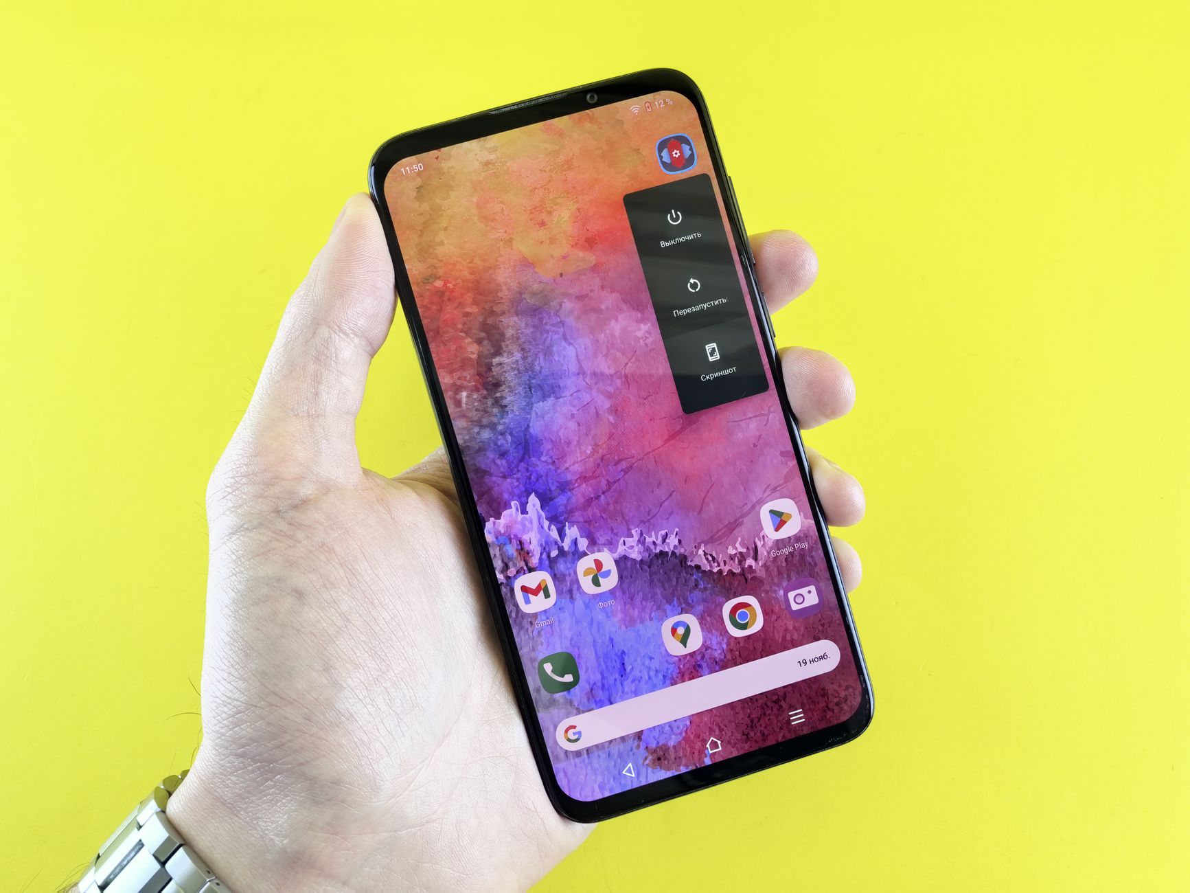 Burn-in em tela OLED: qual é o risco em 2026? A close-up of a hand holding a smartphone with a colorful abstract wallpaper against a yellow background.