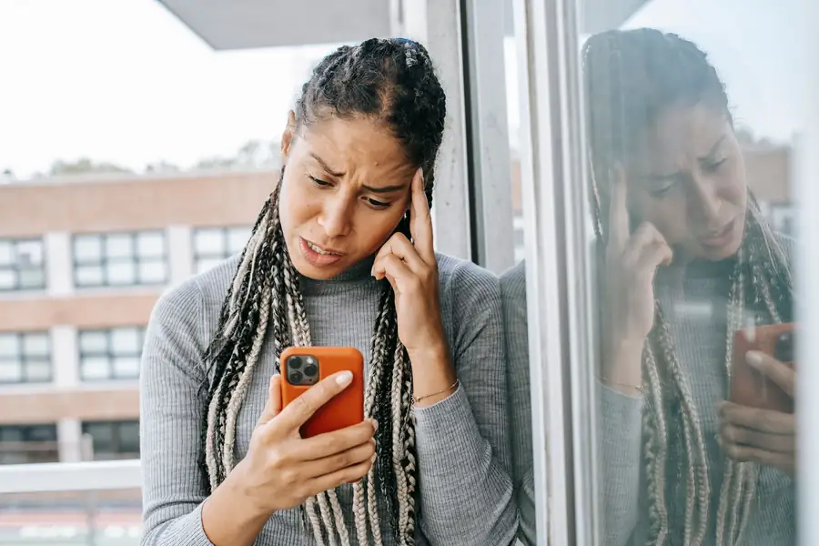 Mulher olhando a tela do smartphone com expressão de frustração em uma varanda Mulher olhando a tela do smartphone com expressão de frustração em uma varanda
