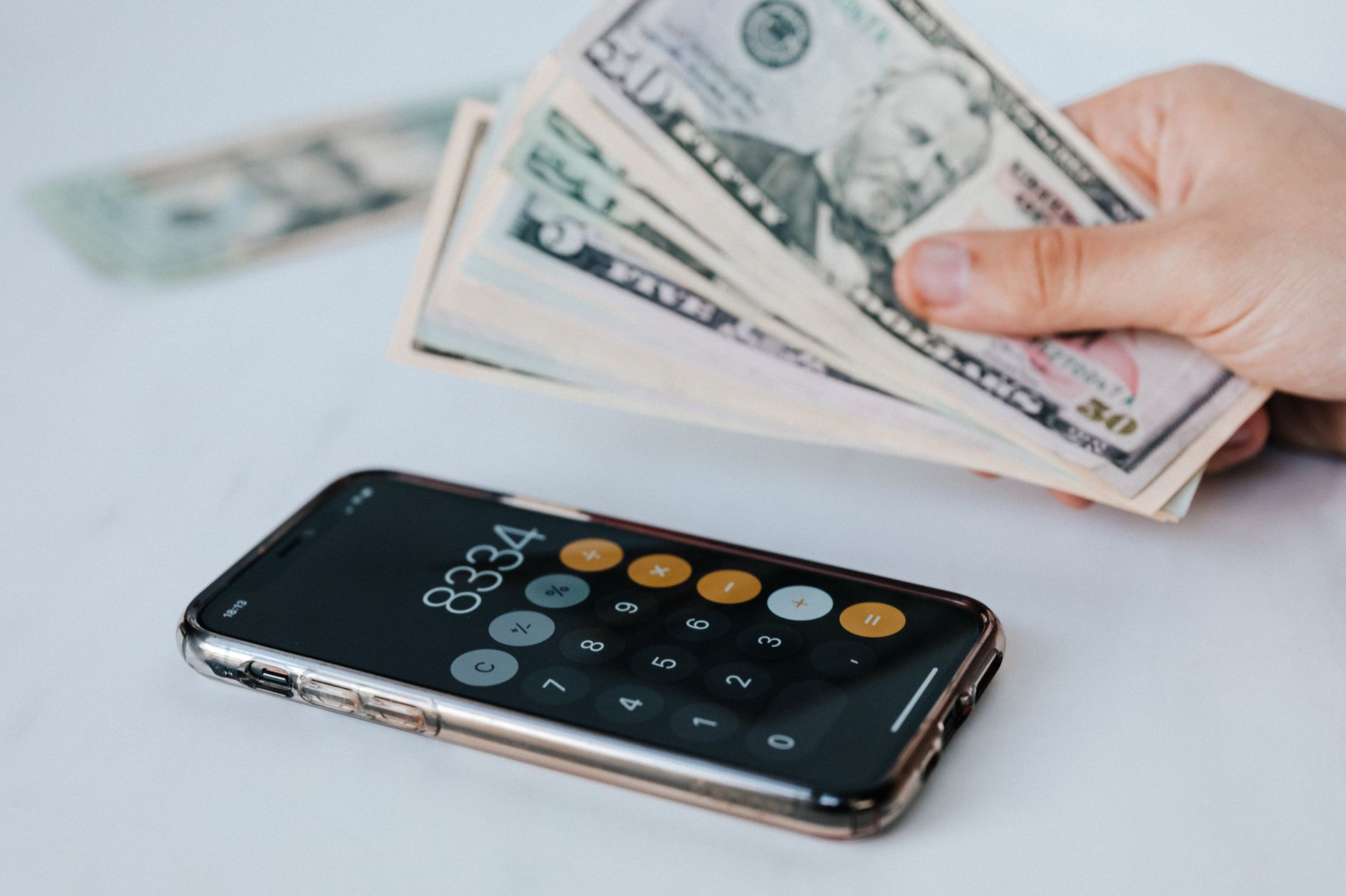 Pessoa conferindo a conversão entre dólares e euros em uma mesa com celular e documentos.