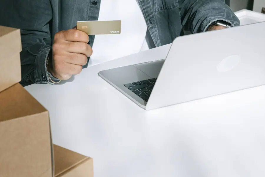 Pessoa pagando uma compra on-line com cartão de crédito diante de caixas de entrega Pessoa pagando uma compra on-line com cartão de crédito diante de caixas de entrega