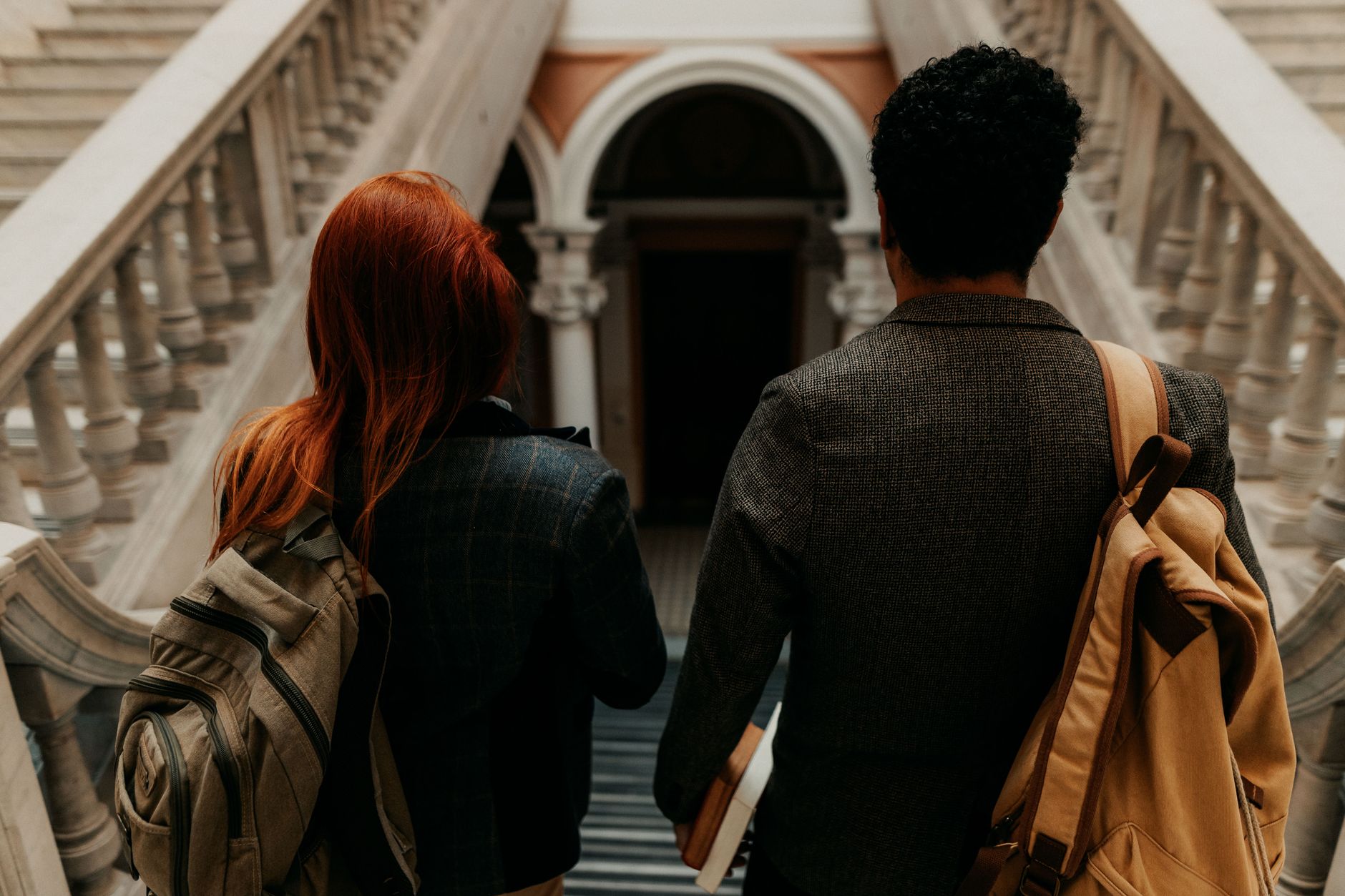 Estudante caminhando pelo campus de uma universidade europeia tradicional carregando livros e mochila.