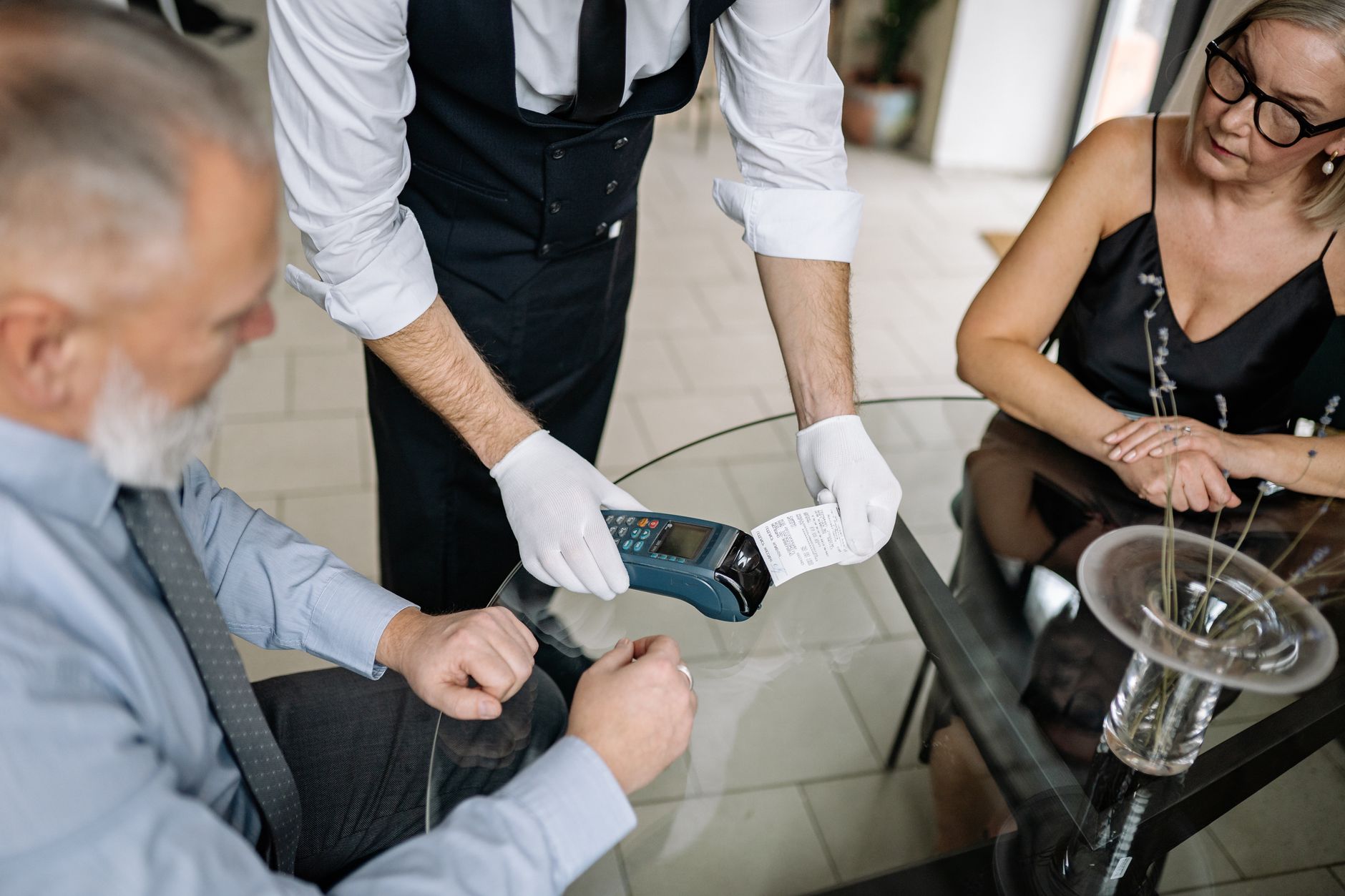 Qual é o IOF do cartão internacional? Entenda como funciona A couple making a contactless payment using a credit card at a restaurant table.