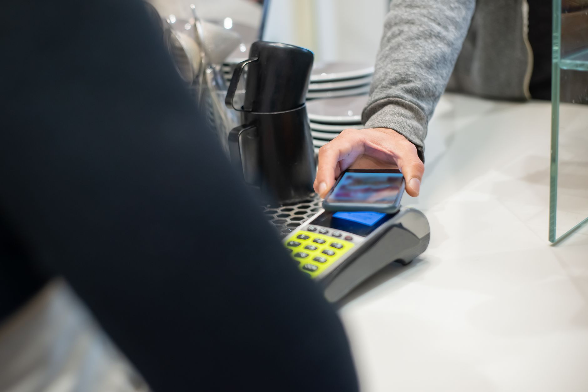 Como funciona o cartão pré-pago em euros? A customer makes a contactless payment using a smartphone at a café, showcasing modern digital transactions.