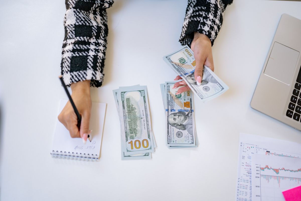 Pessoa analisando gráficos de investimentos com cédulas de dólar e calculadora sobre a mesa