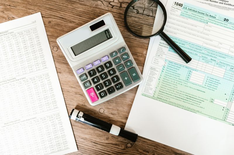 Como Declarar Dólar em Espécie Guardado em Casa no IR Top view of tax forms, a calculator, and a magnifying glass on a wooden surface, ideal for accounting themes.