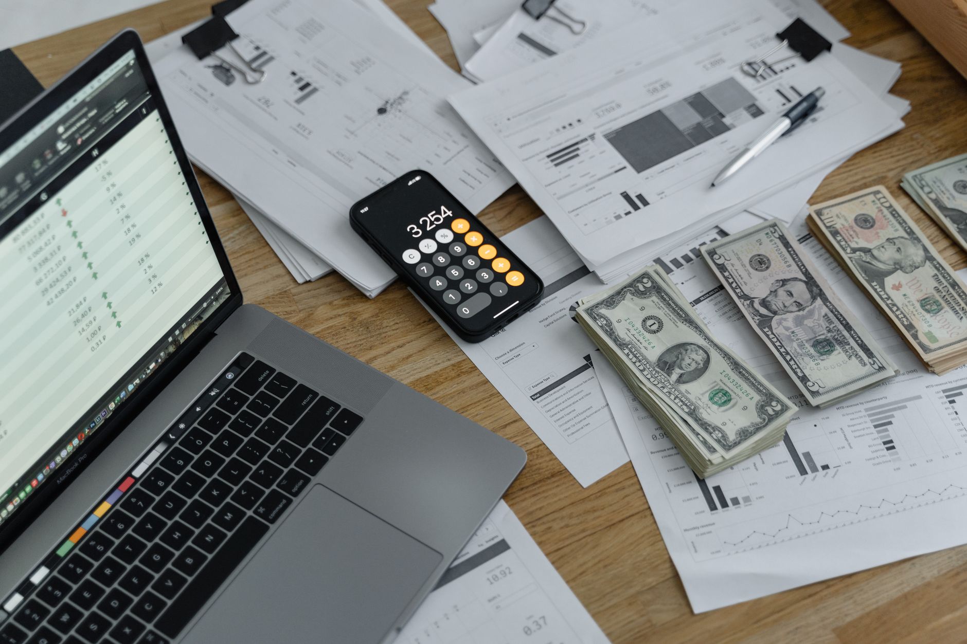 Como declarar saldo em dólar de cartão internacional no IR A desk with financial documents, currency, a laptop, and phone calculator.