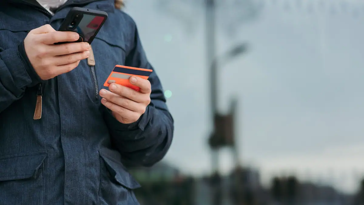 Pessoa usando um cartão e um smartphone na rua para pagamentos online