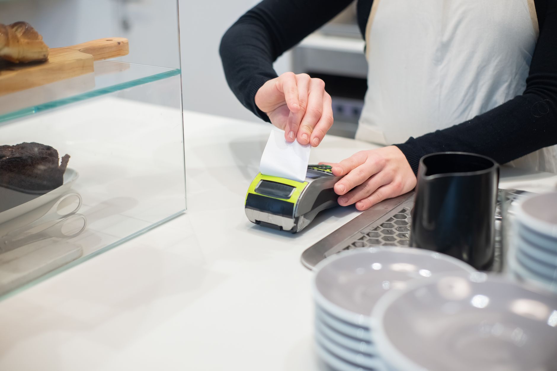 Como funciona a cobrança em moeda local (DCC) e por que evitar Close-up of a cashless transaction at a modern café counter with hands holding a receipt.