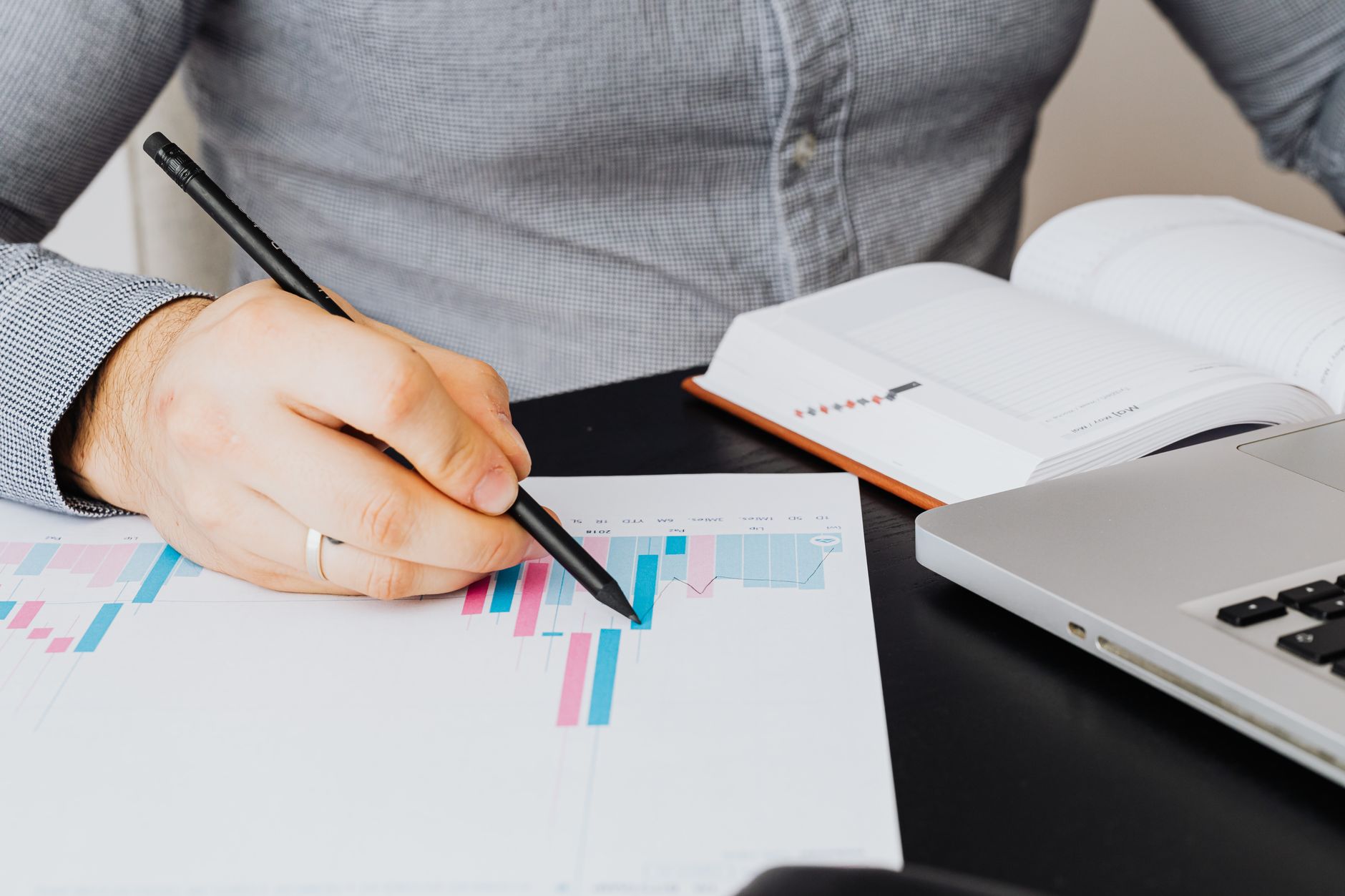 Pessoa analisando extratos e documentos financeiros em um notebook sobre a mesa de escritório.