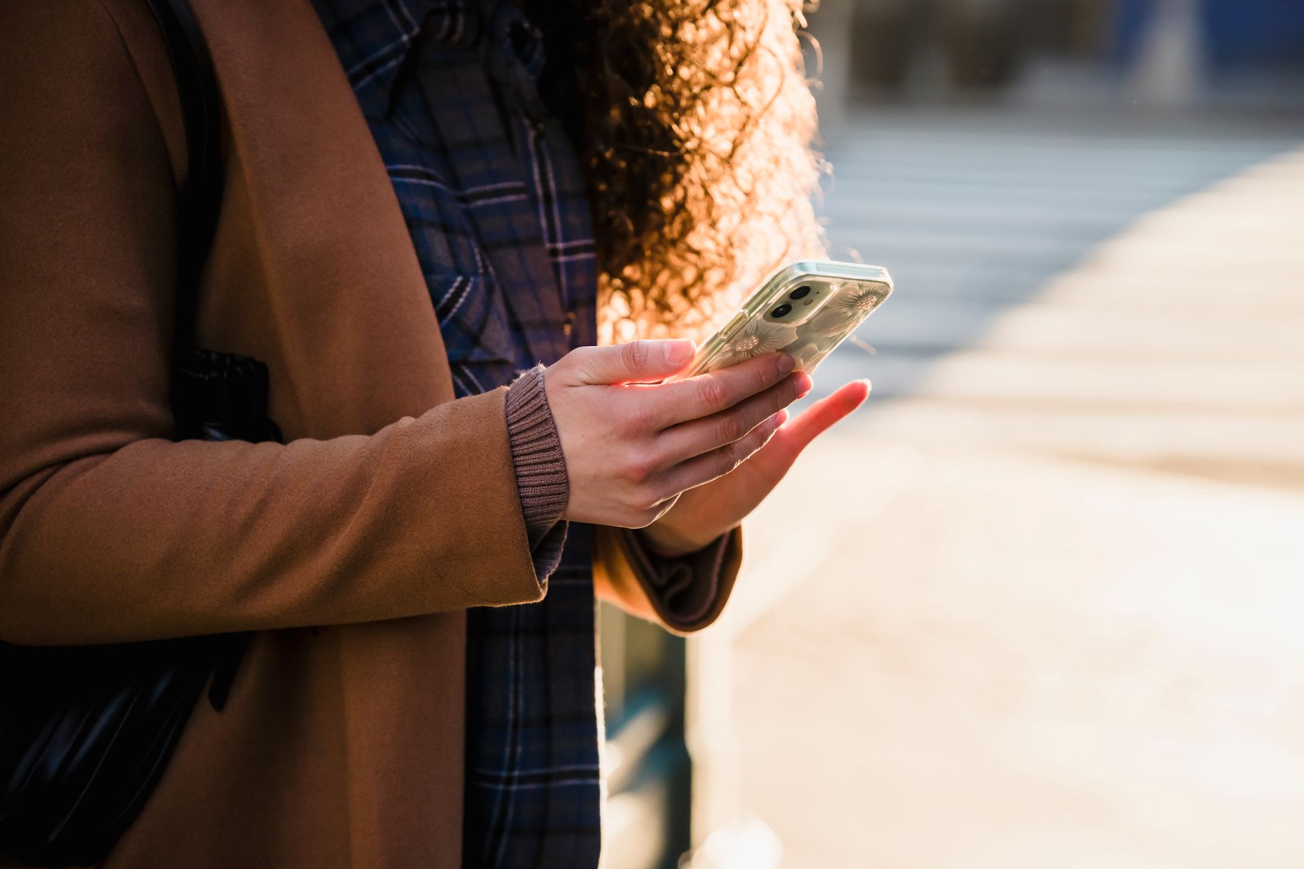Como Funciona o Cartão Internacional para Gastar em Euros Crop anonymous female with curly hair in warm stylish coat using mobile phone on blurred background of urban street