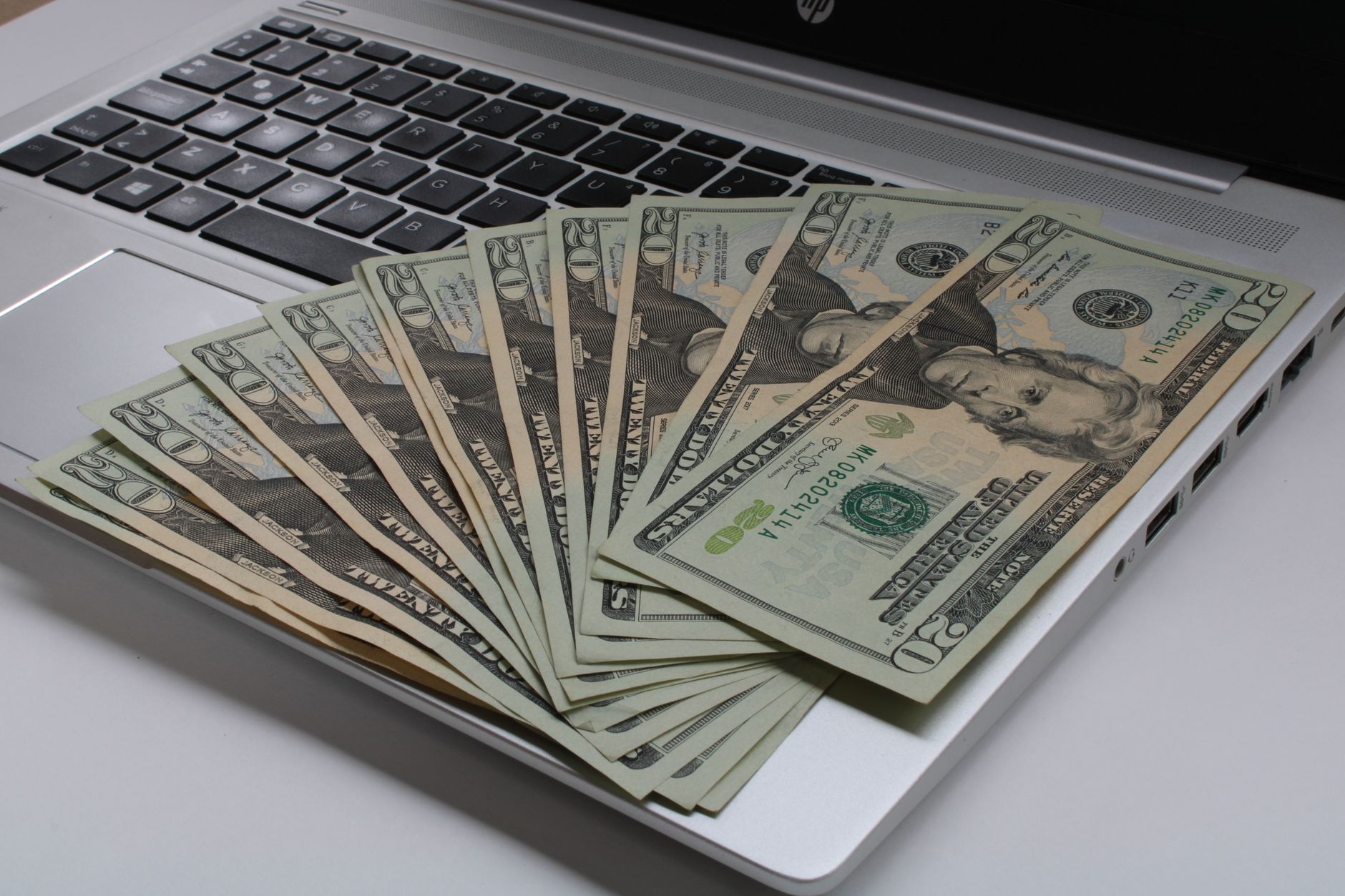 Como funciona o imposto para quem recebe salário em dólar Stack of US dollar bills fanned out on a laptop keyboard, symbolizing online finance.