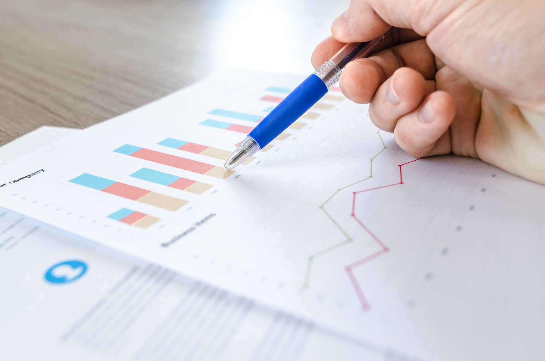 Pessoa analisando gráficos econômicos e uma tela com a cotação do dólar em uma mesa de trabalho