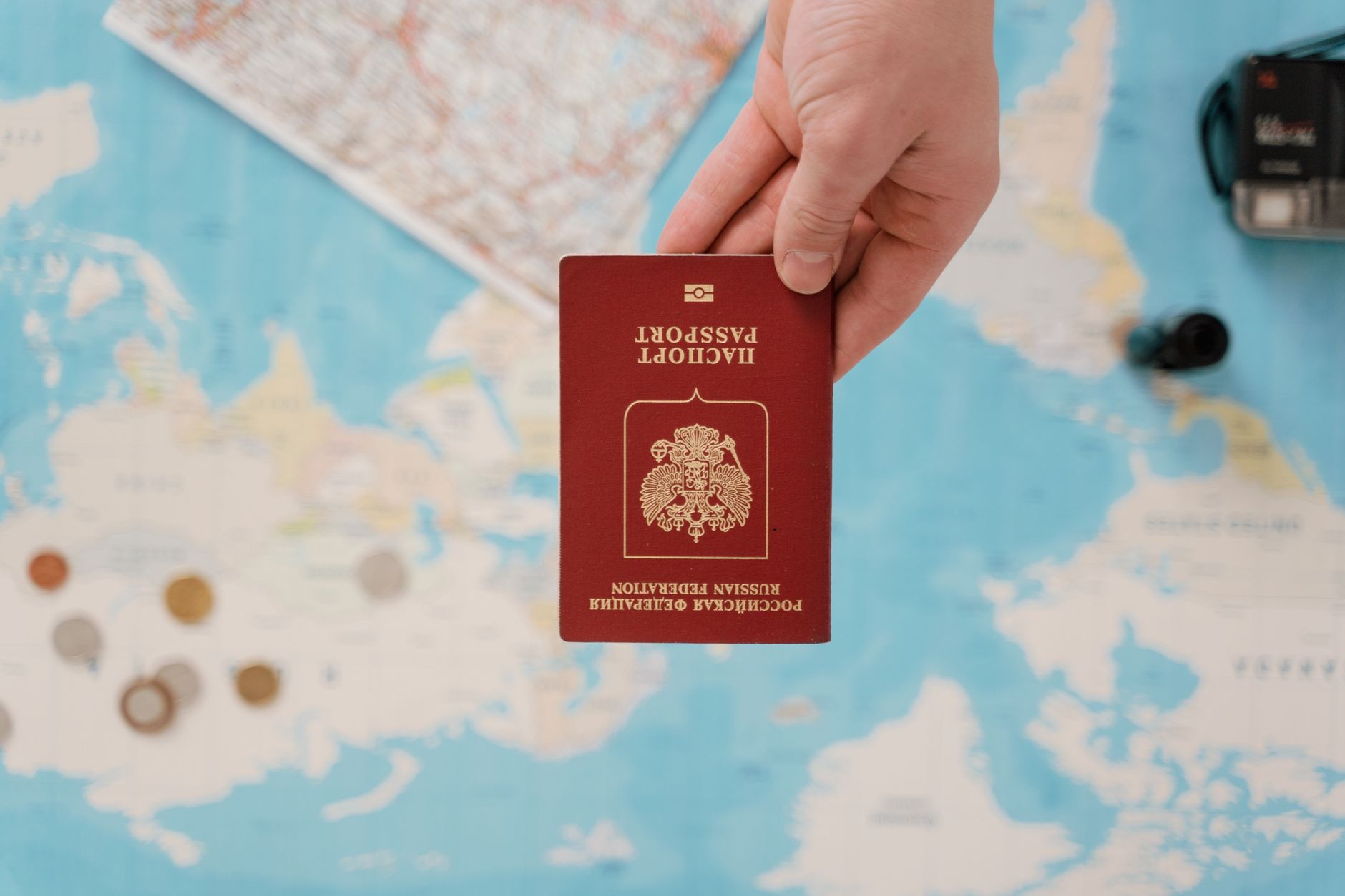 Pessoa organizando notas de moedas estrangeiras, passaporte e calculadora sobre uma mesa de madeira.