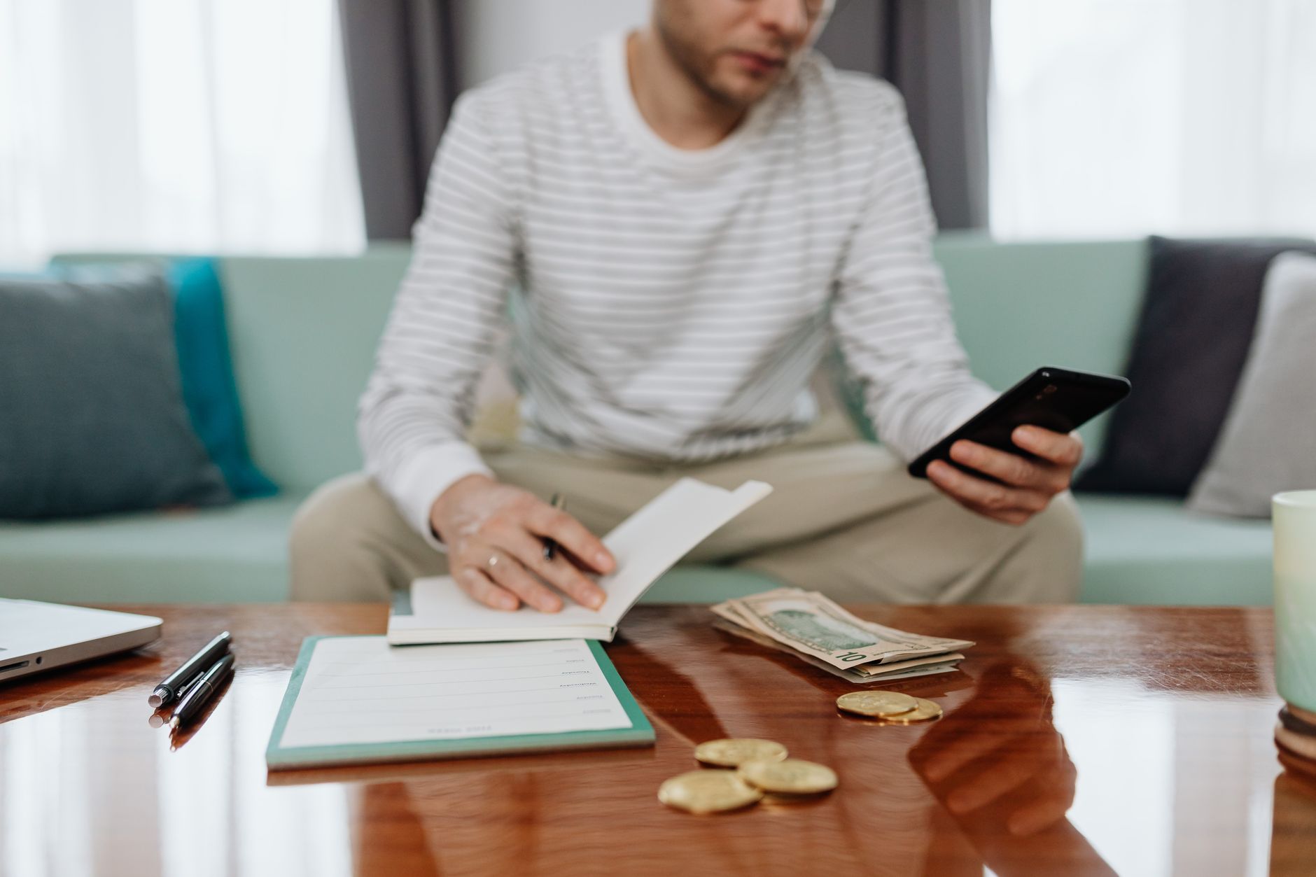 Como receber pagamento em dólar do exterior sendo freelancer Adult man sits on sofa managing finances with cash, smartphone, and notebook.