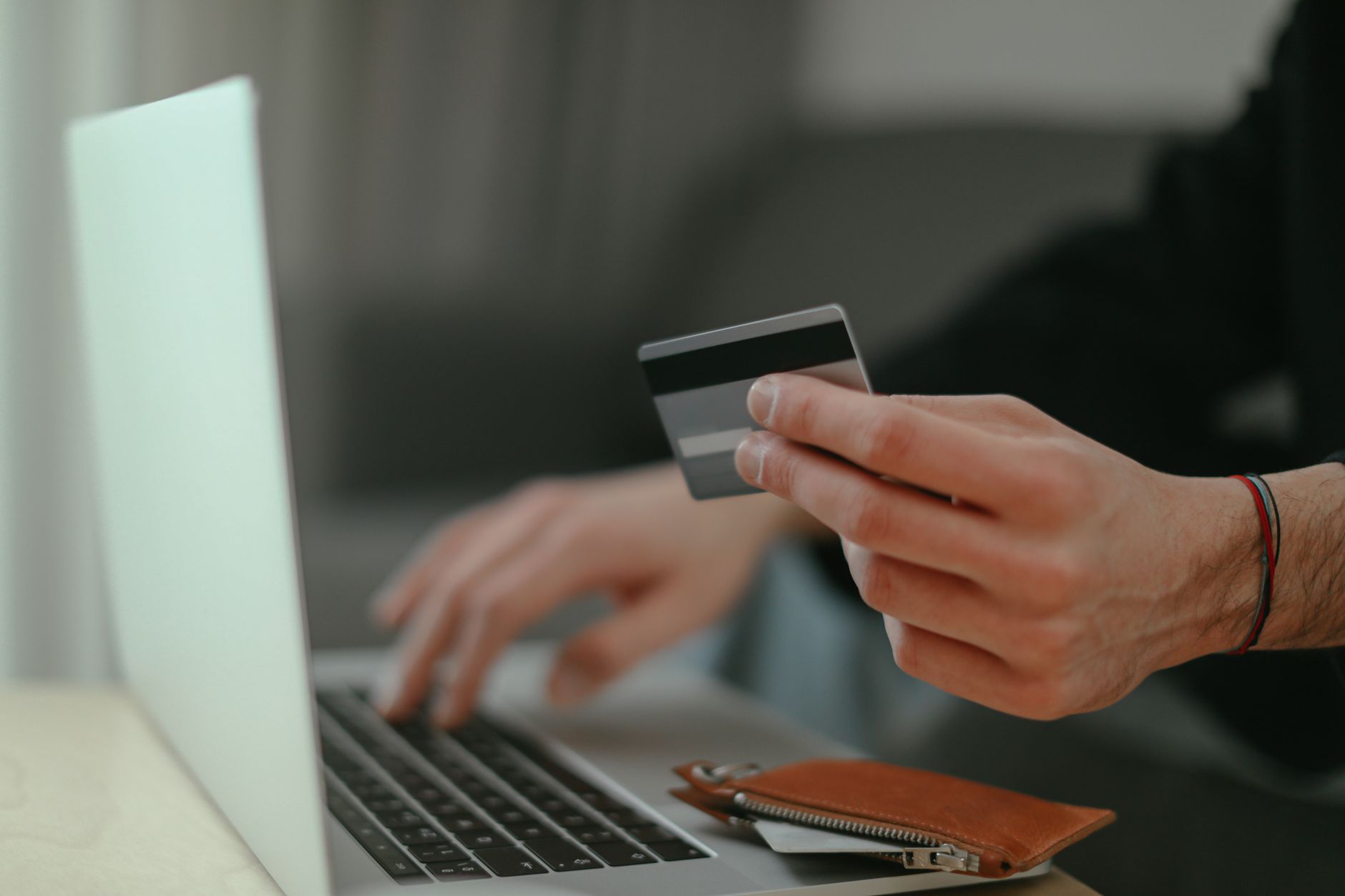 Como usar o cartão internacional em assinaturas estrangeiras Close-up of a person holding a credit card while shopping online on a laptop.