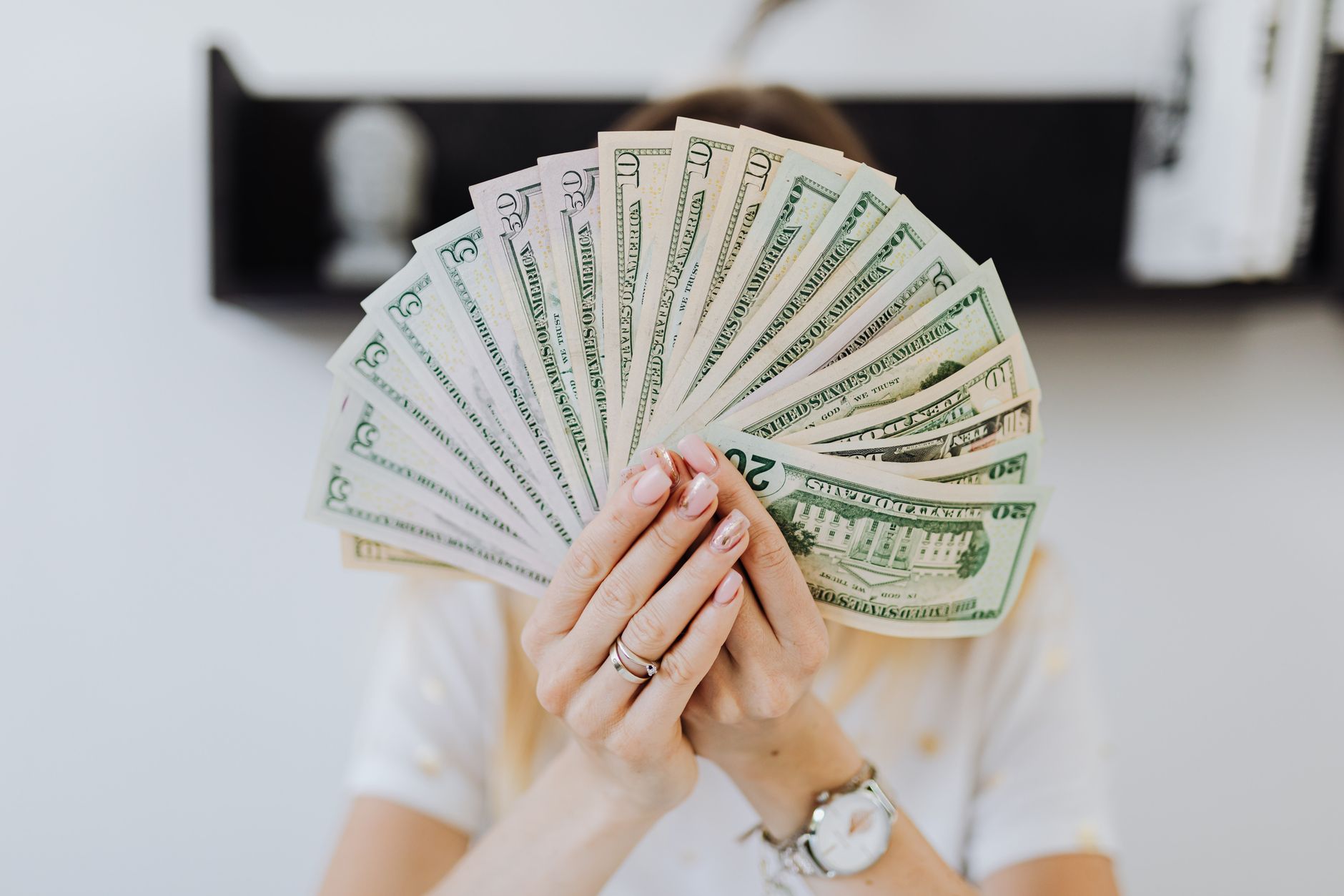 Pessoa segurando passaporte, moedas e notas de dólar sobre uma mesa.