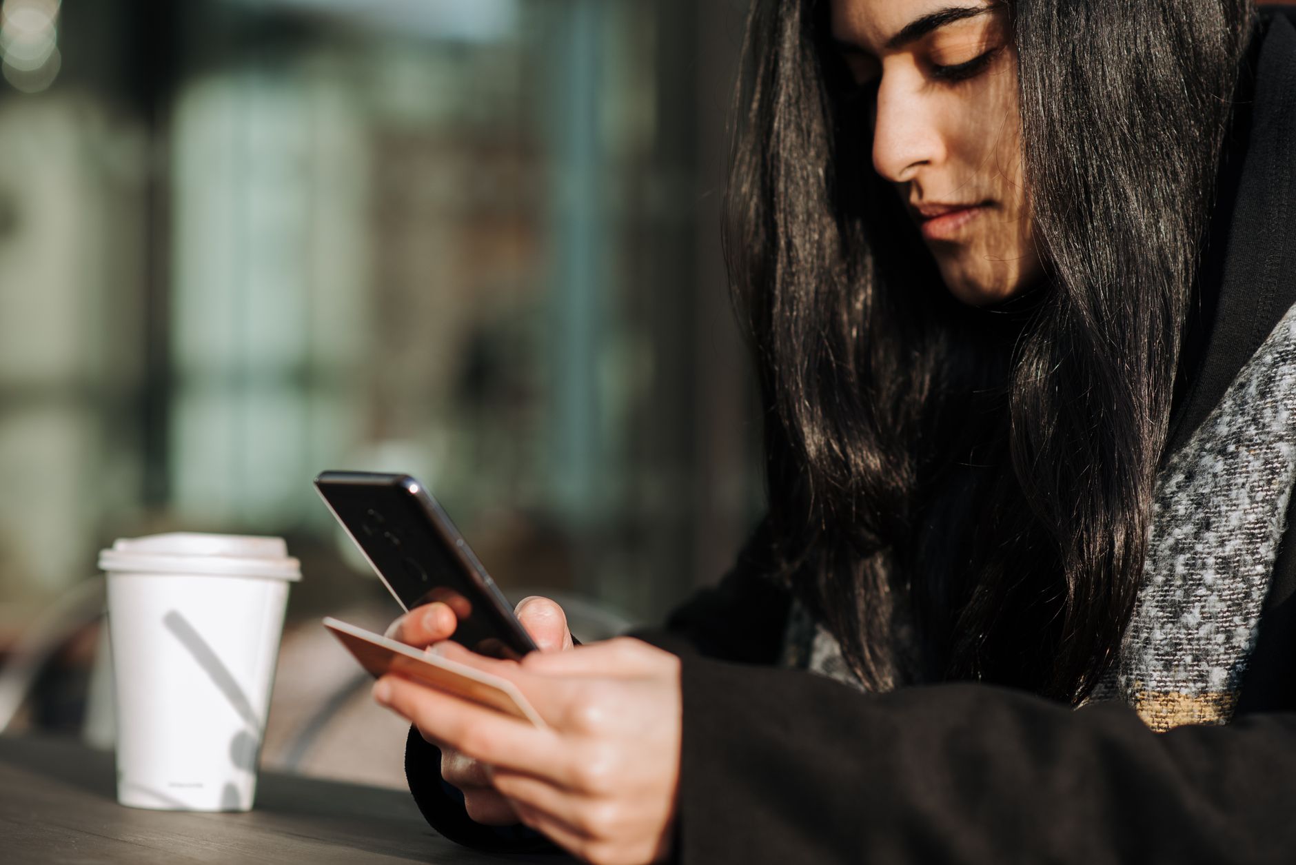 Casal sentado em uma mesa de café analisando um celular e cartões de débito internacionais sobre a mesa.