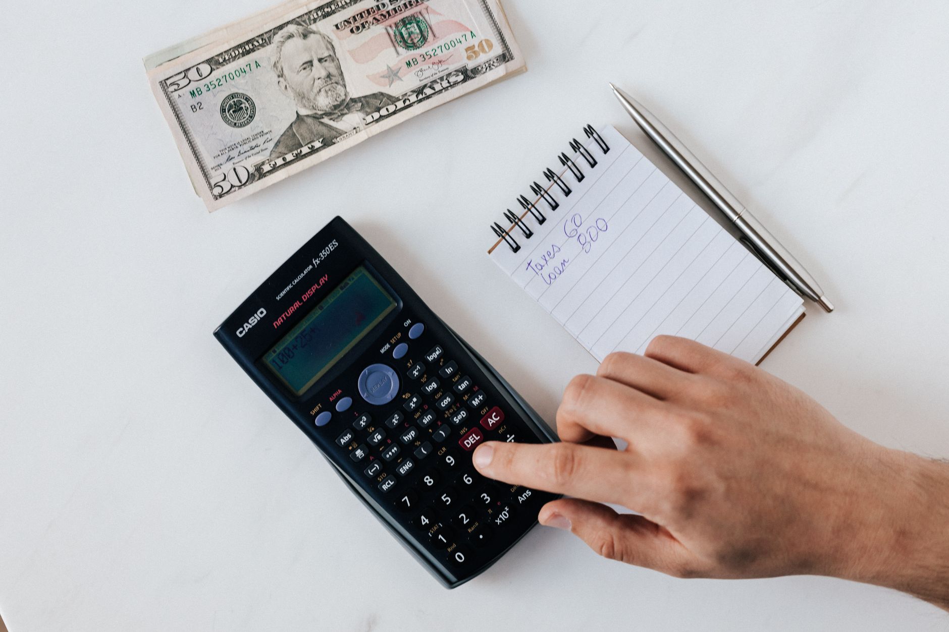 Qual é o custo total para comprar euro? Top view of crop unrecognizable economist calculating on calculator on table with notepad and pen near pile of dollar banknotes on marble table