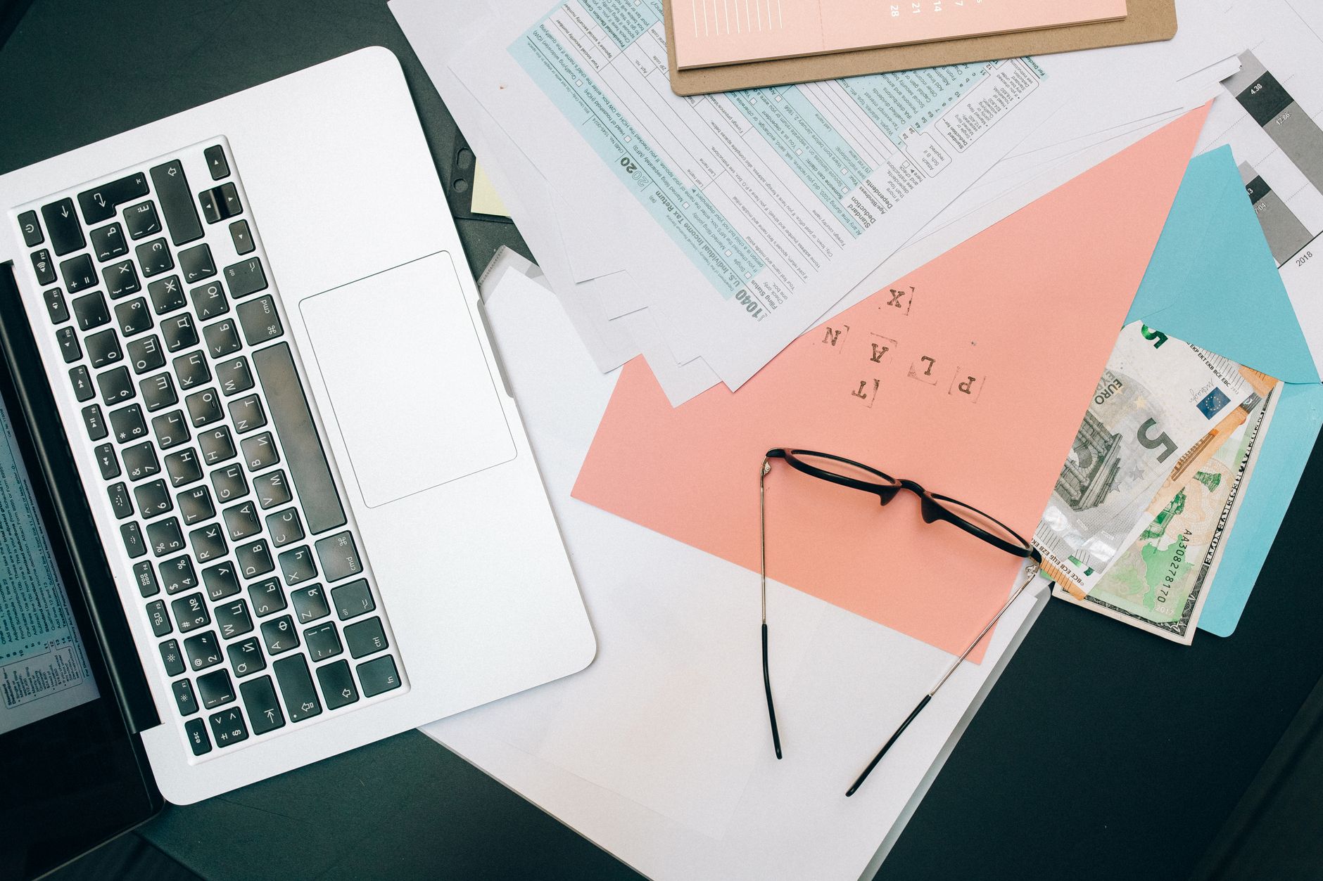 Como Declarar Investimento em Euro no Imposto de Renda A tidy workspace featuring a laptop, documents, and eyeglasses for productivity.