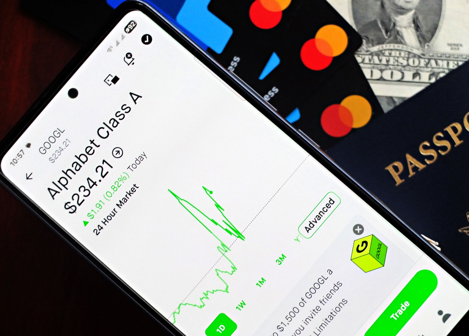 Dólar direto ou fundo: entenda as diferenças Smartphone displaying stock market app next to U.S. dollar and passport, representing global finance.