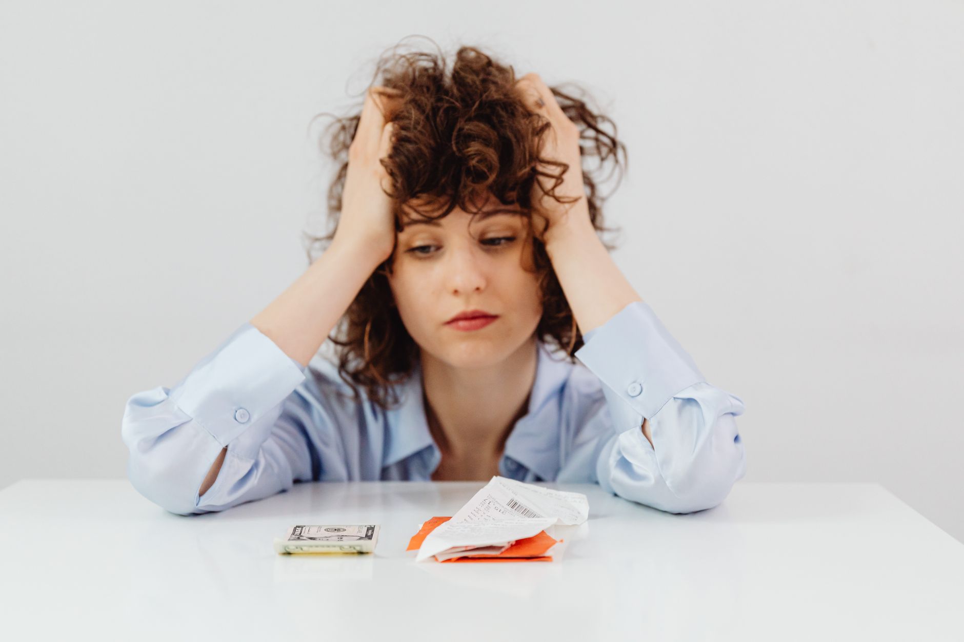 Dólar comercial x dólar turismo: entenda a diferença Woman in blue sleeves appears stressed while looking at receipts and money, symbolizing financial stress.