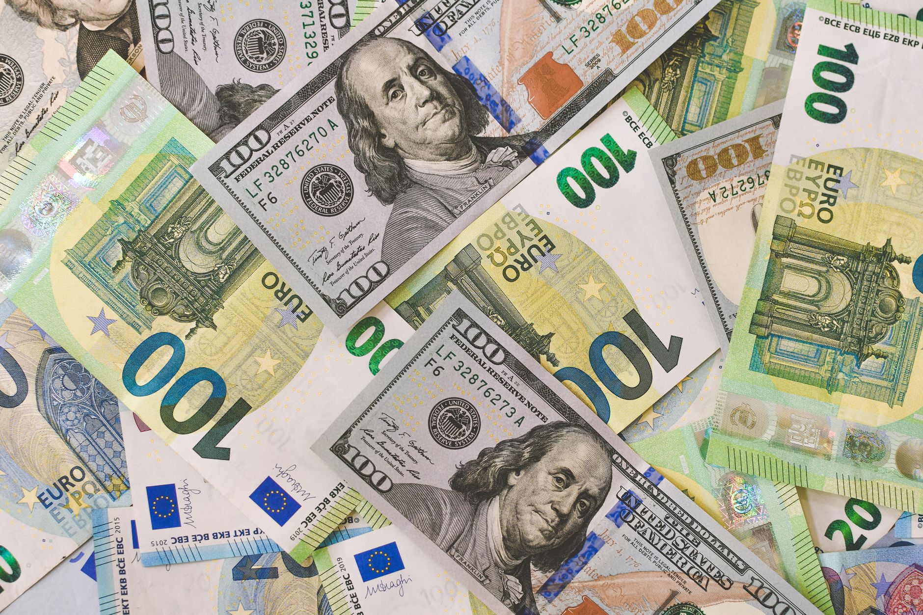 Pessoa comparando cédulas de dólar e euro sobre uma mesa