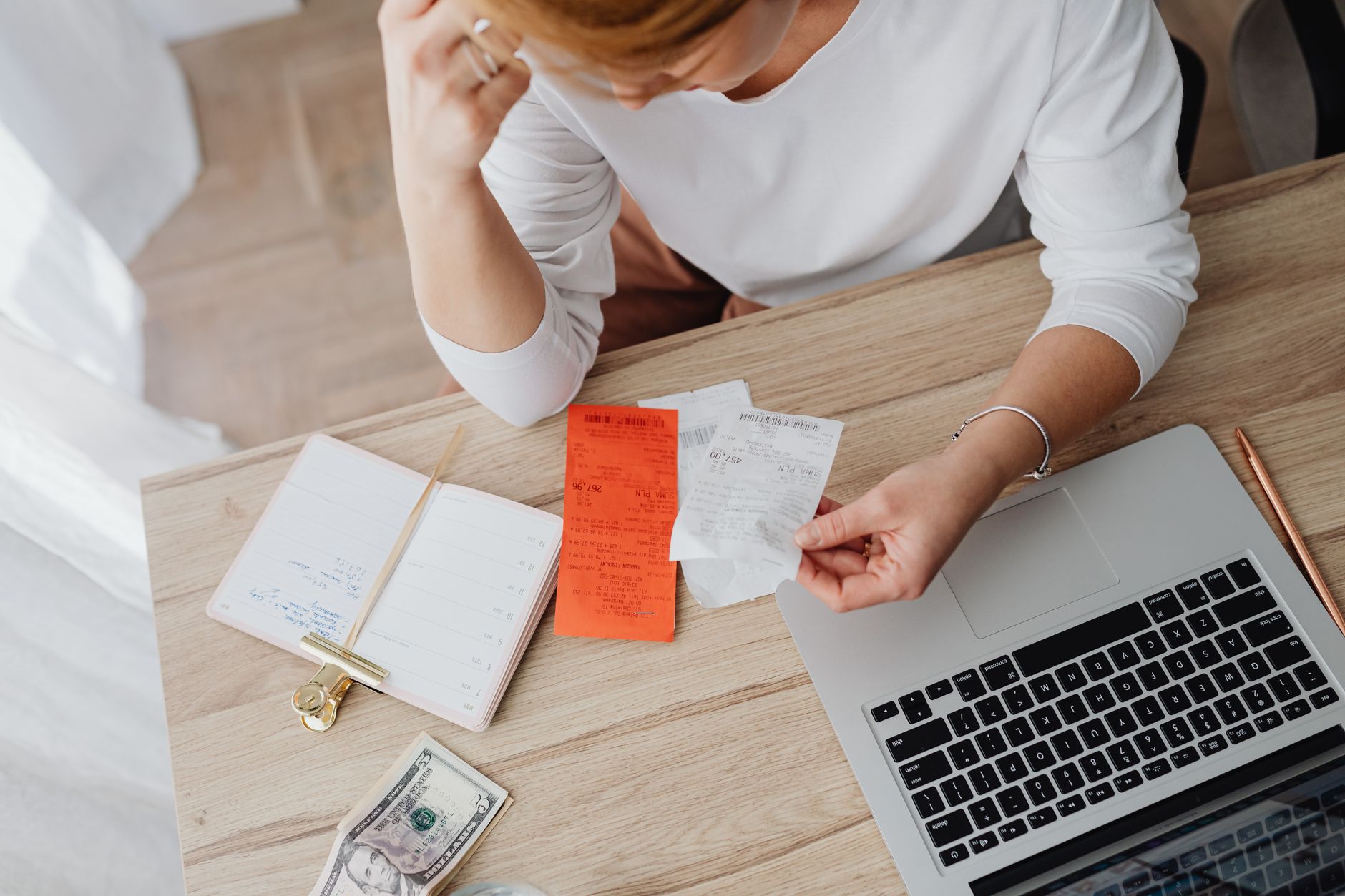 Dólar e euro: qual é a diferença entre as moedas? Woman reviewing receipts and planning budget using a laptop and notebook at home to manage expenses.