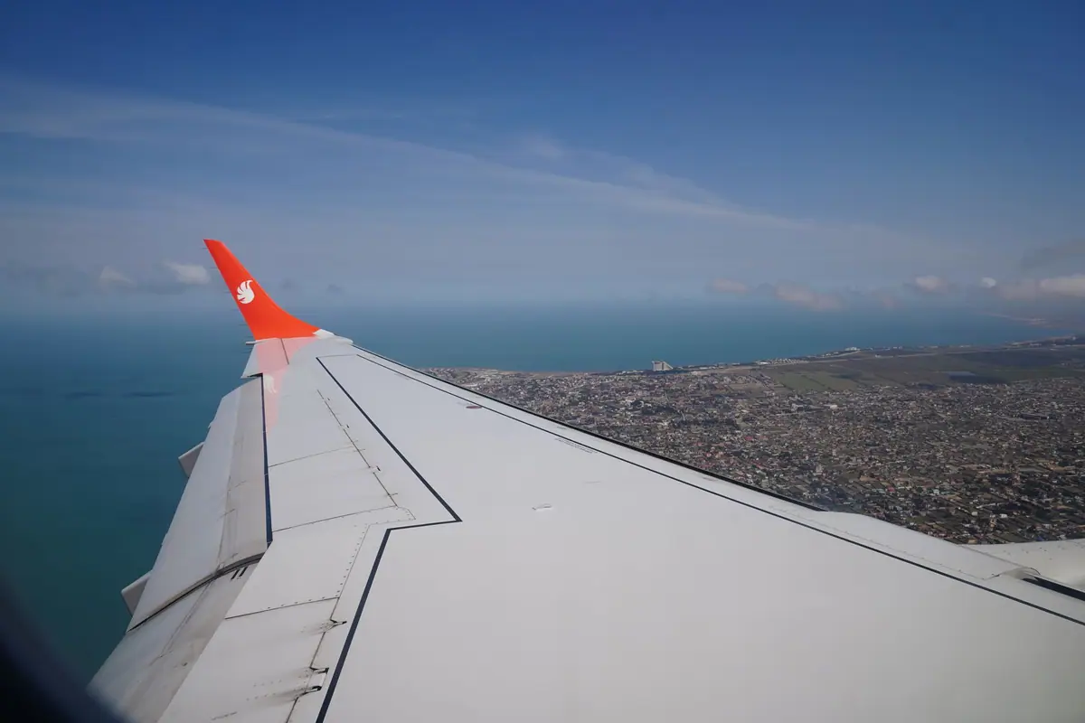 Vista da asa de um avião e de uma cidade litorânea pela janela