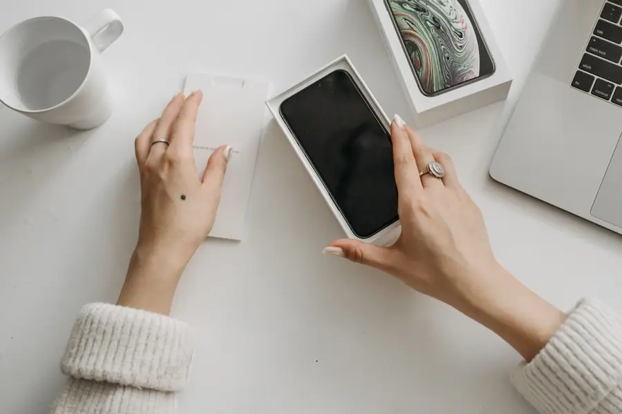 Mulher abrindo a caixa de um smartphone novo sobre uma mesa branca