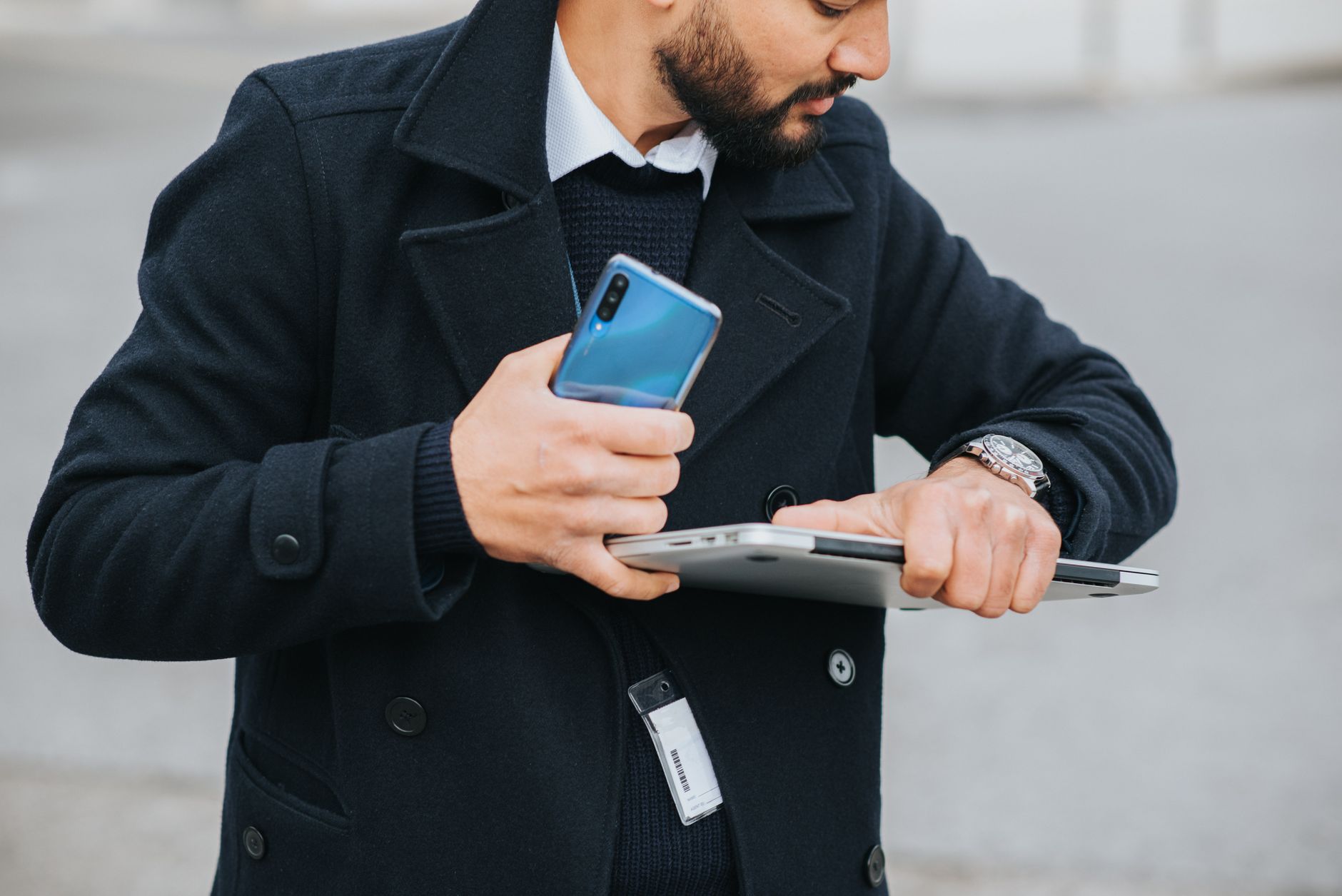 Como converter dólar para euro sem errar? Crop attentive ethnic male office worker in formal apparel with smartphone and laptop checking time on wristwatch in city