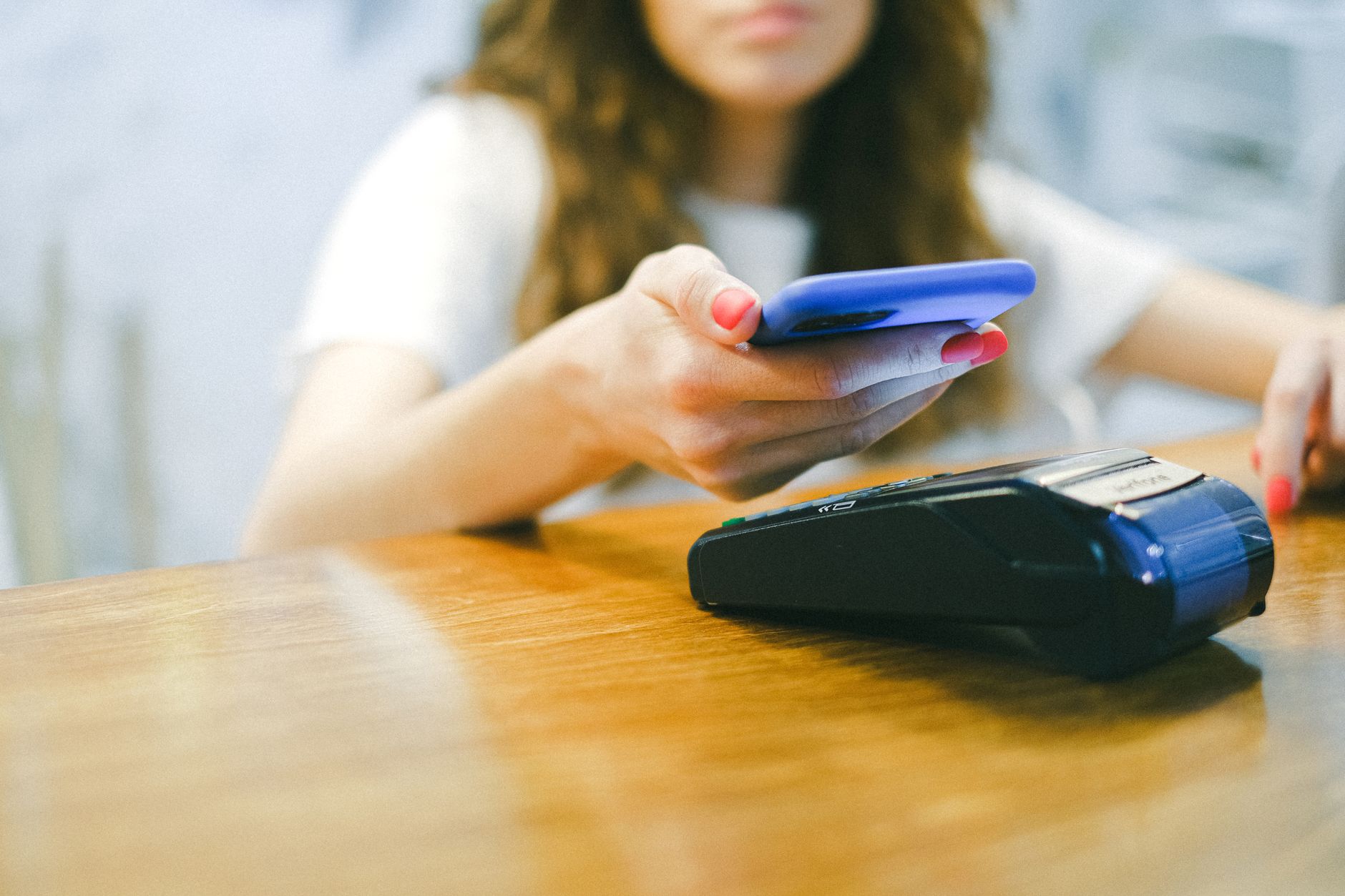 Dólar, euro e real: como comparar as três moedas? A woman processes a contactless payment using her smartphone at a payment terminal.