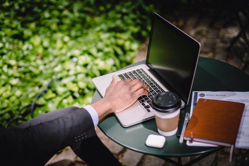 Dólar Futuro na B3: Entenda os Riscos do Mini Contrato High angle of crop anonymous young man in formal suit typing on laptop while sitting at round table with coffee notebook and documents in outdoor cafe