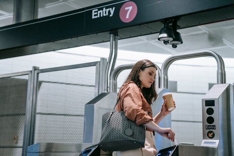 Erros ao guardar dólar no pânico e como evitar A woman holding coffee enters a train station through a turnstile at Entry 7.