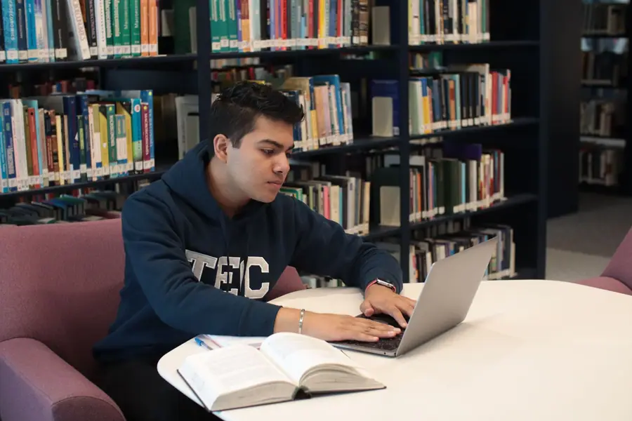 Estudante usando notebook e livros em uma biblioteca Estudante usando notebook e livros em uma biblioteca