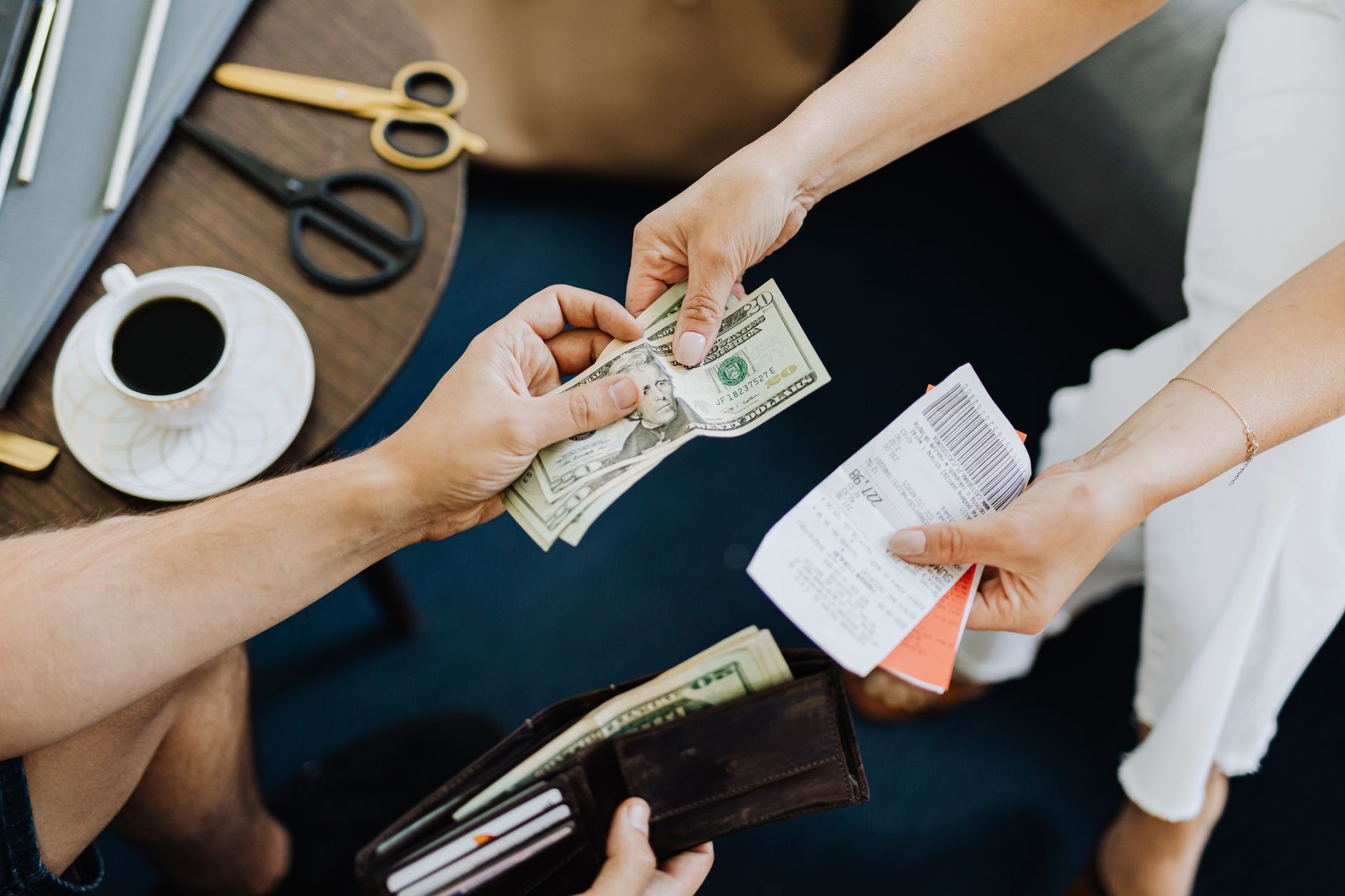 Euro na Bélgica: como pagar durante a viagem Close-up of a transaction with US dollar bills and receipts being exchanged over a table with coffee and scissors.