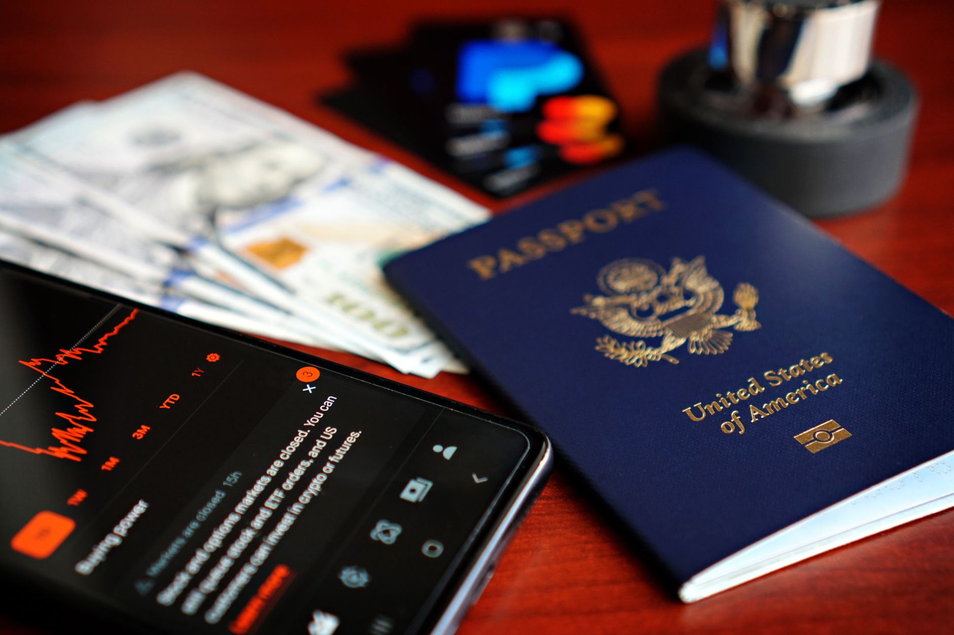 Pessoa segurando notas de euro e um passaporte ao lado de um cartão de crédito sobre a mesa.