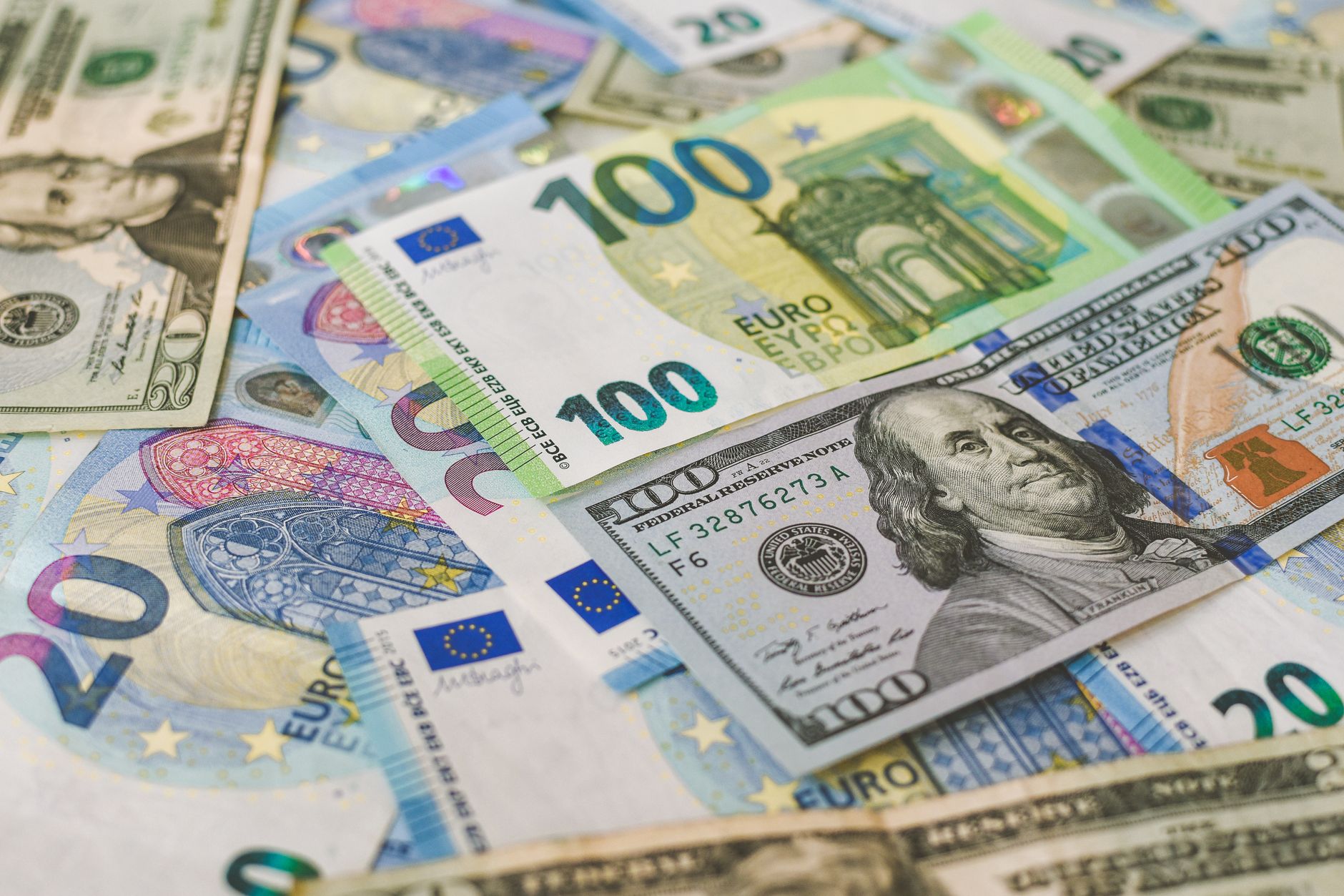 Notas de euro e notas de dólar dispostas sobre uma mesa de madeira ao lado de um passaporte e um mapa.