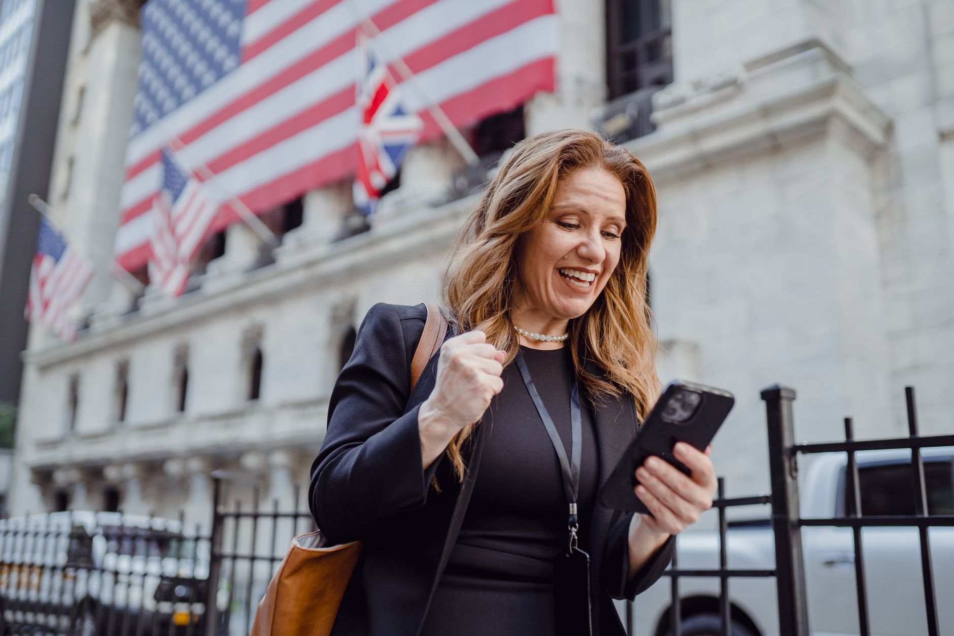 Euro dólar hoje: entenda a cotação EUR USD Smiling woman celebrates success while checking mobile phone near iconic city building with flags.