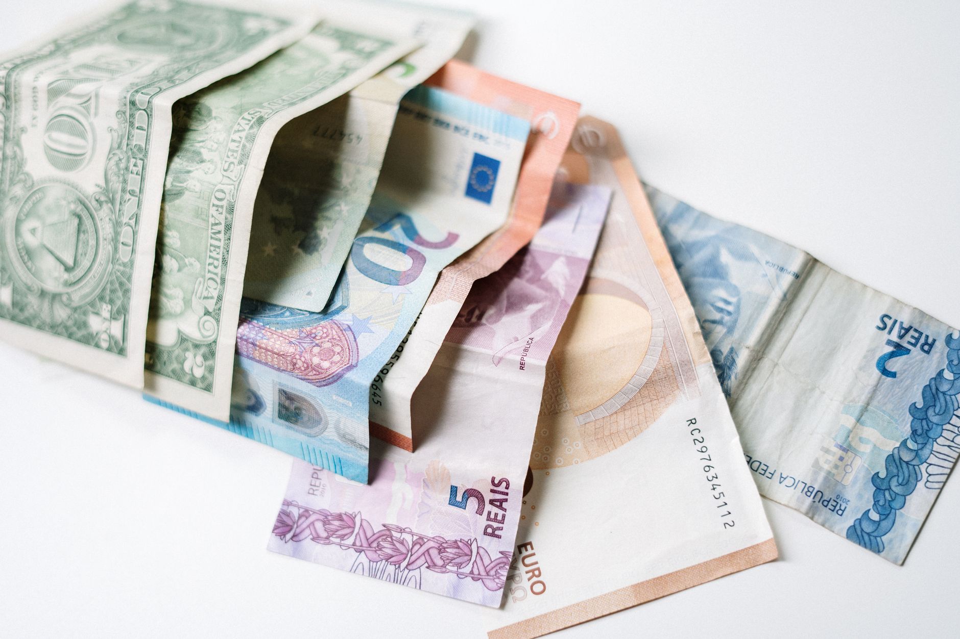 Pessoa segurando notas de euro e dólar em equilíbrio.