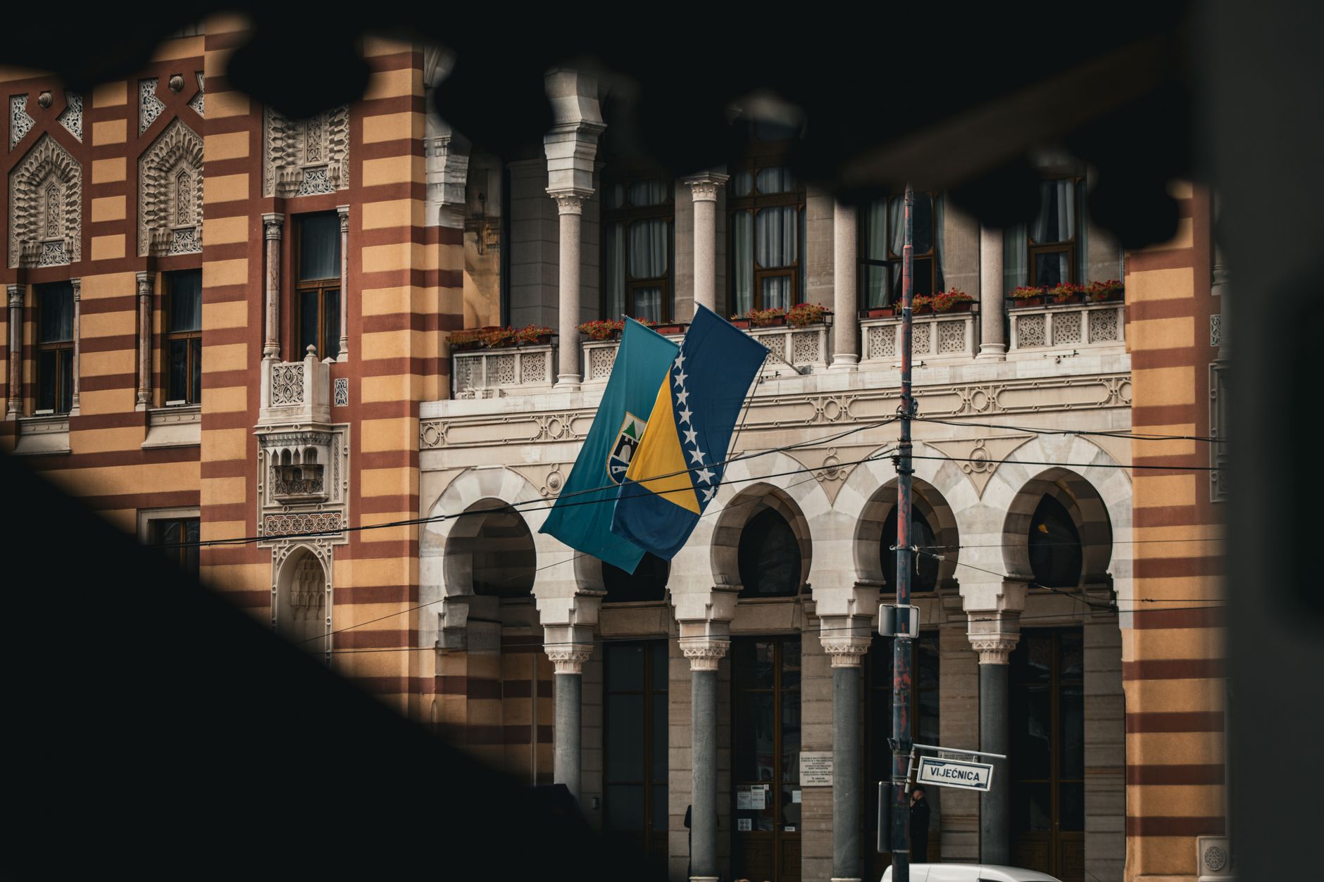 Como conflitos internacionais afetam o euro? Beautiful view of Sarajevo City Hall with the national flag of Bosnia and Herzegovina.