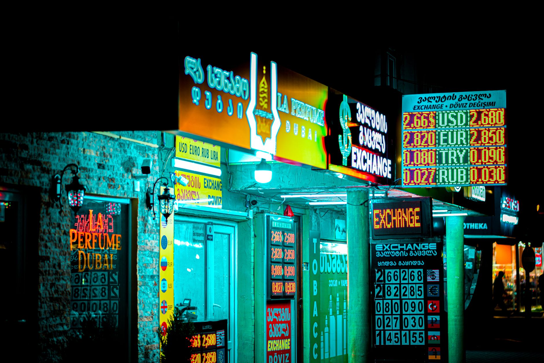Como a inflação afeta o euro? Night view of a brightly lit storefront and currency exchange signs in Batumi, Georgia.