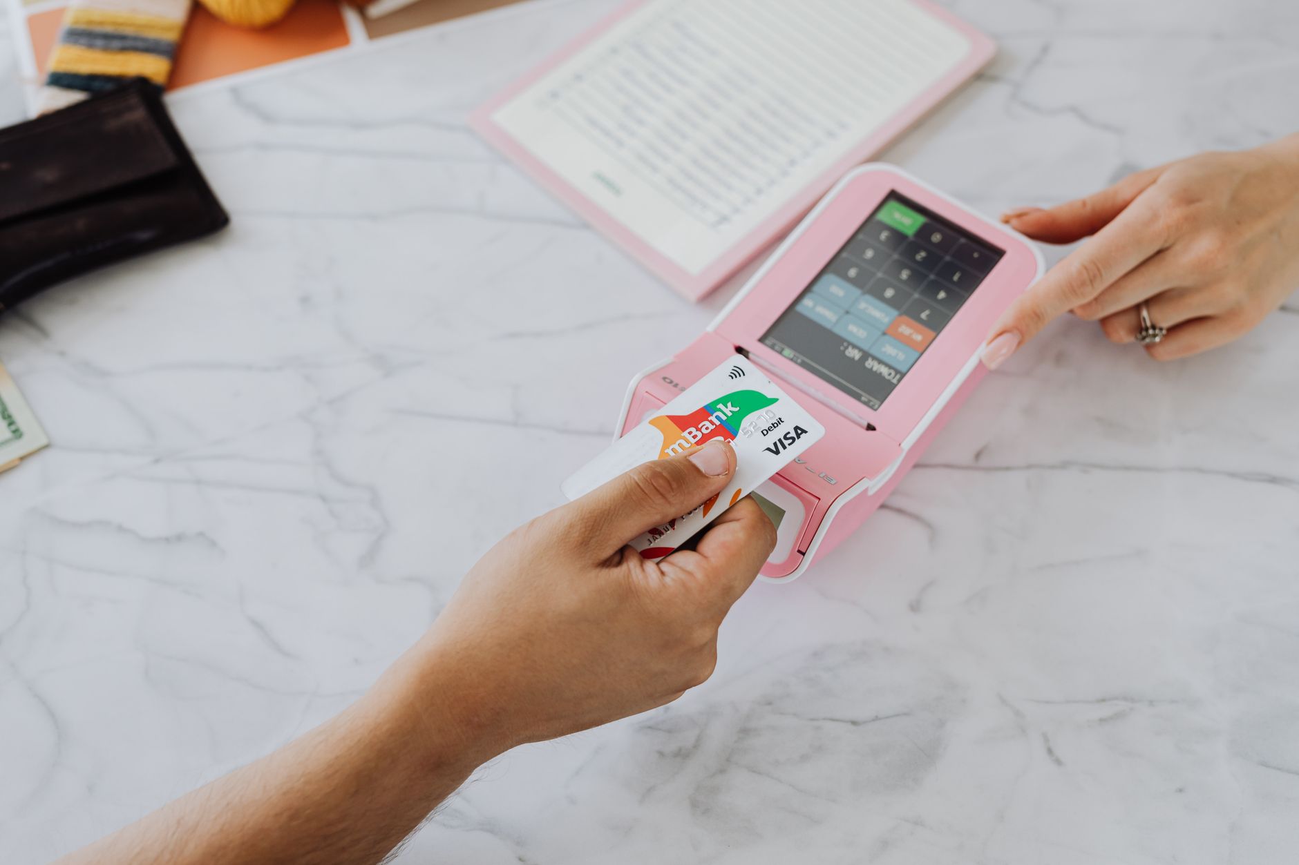 Como a política monetária do Brasil afeta o preço do euro Hands making a contactless payment using a credit card and a pink terminal on a marble table.